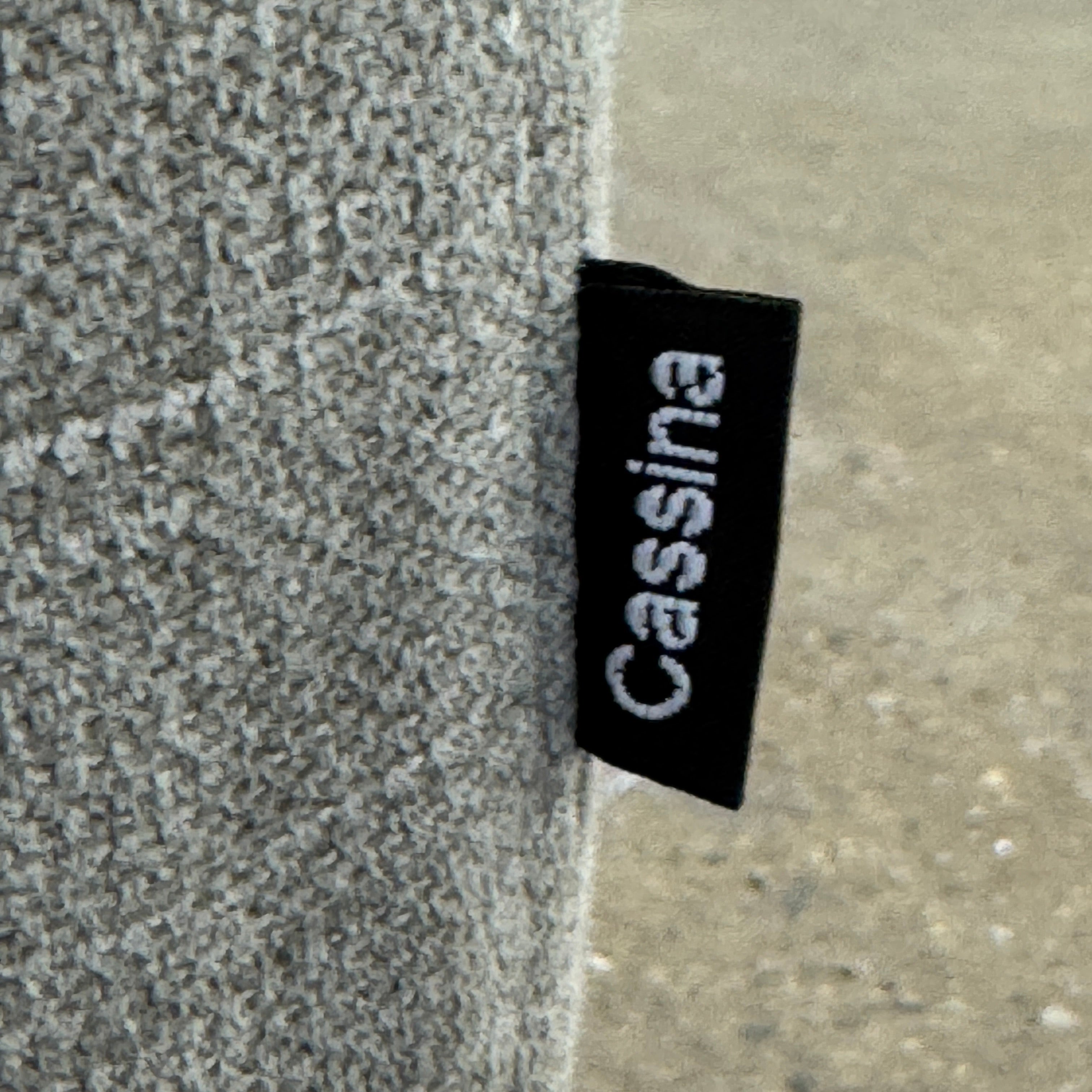 A modern Cassina Scighera Sofa by Cassina, in light gray with two matching square cushions, is placed on a bare concrete floor against a plain white wall.