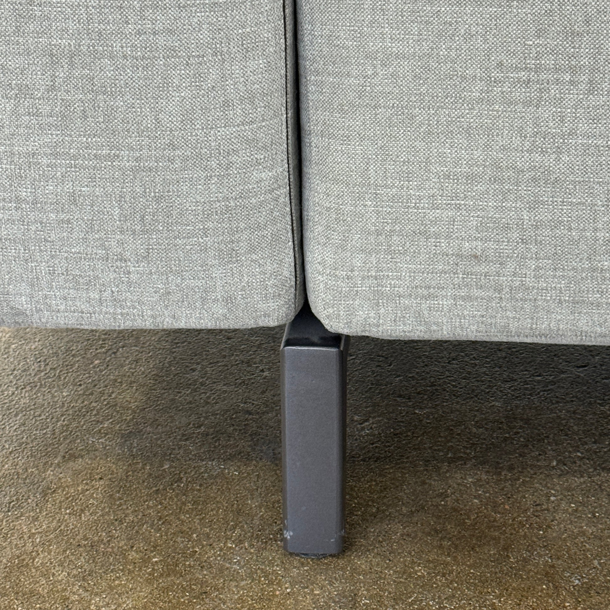 A modern Cassina Scighera Sofa by Cassina, in light gray with two matching square cushions, is placed on a bare concrete floor against a plain white wall.