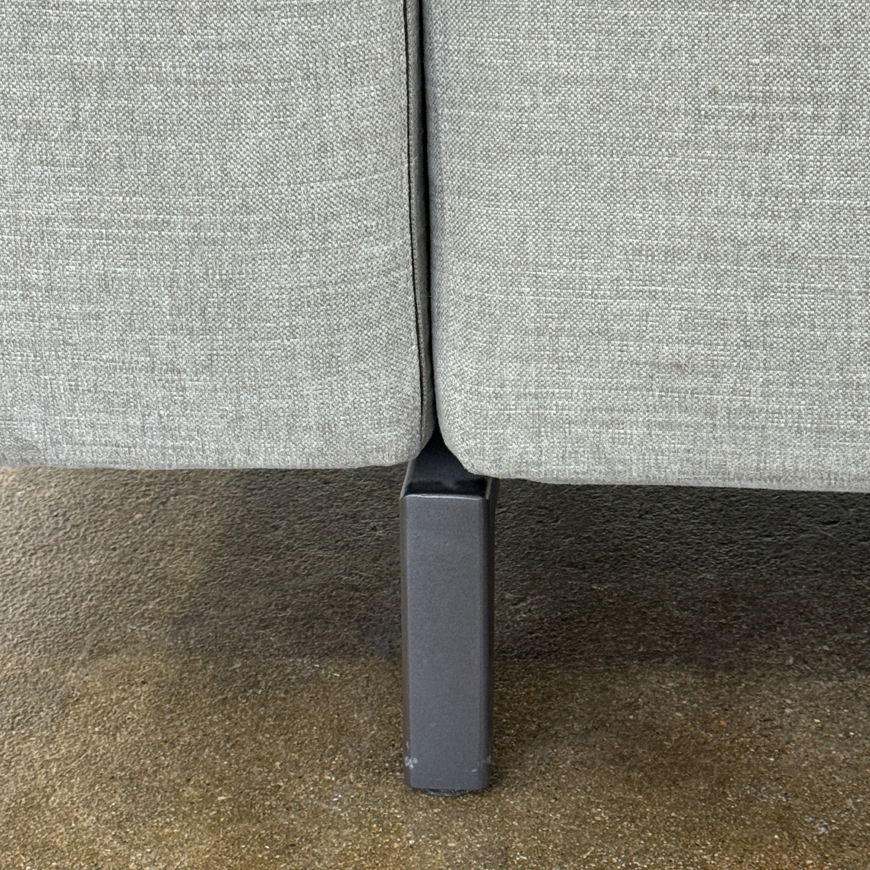 A modern Cassina Scighera Sofa by Cassina, in light gray with two matching square cushions, is placed on a bare concrete floor against a plain white wall.