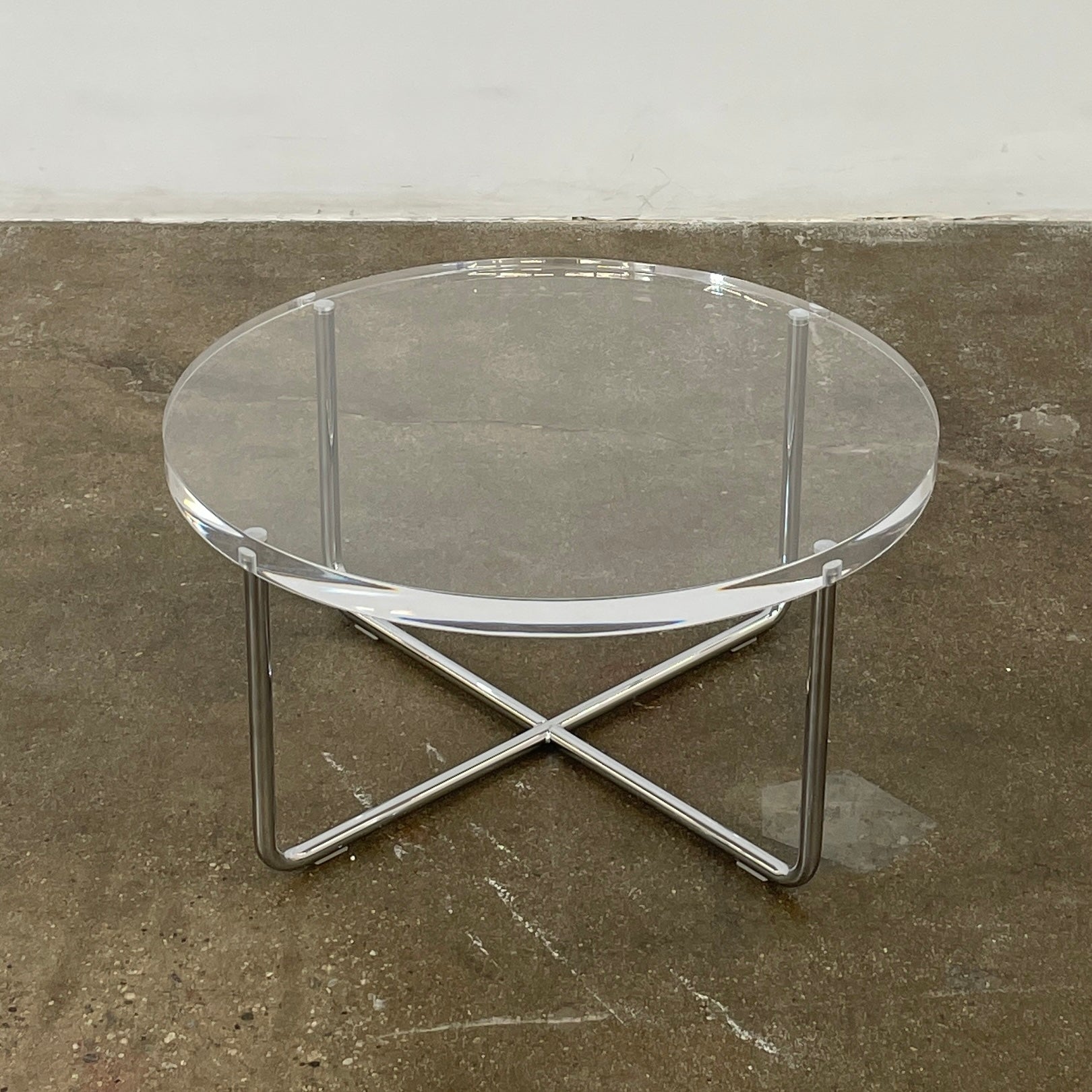 The Minotti Lucite Accent Table boasts a round glass top with a chrome metal frame and crossed base, capturing the Italian elegance synonymous with Minotti's design.