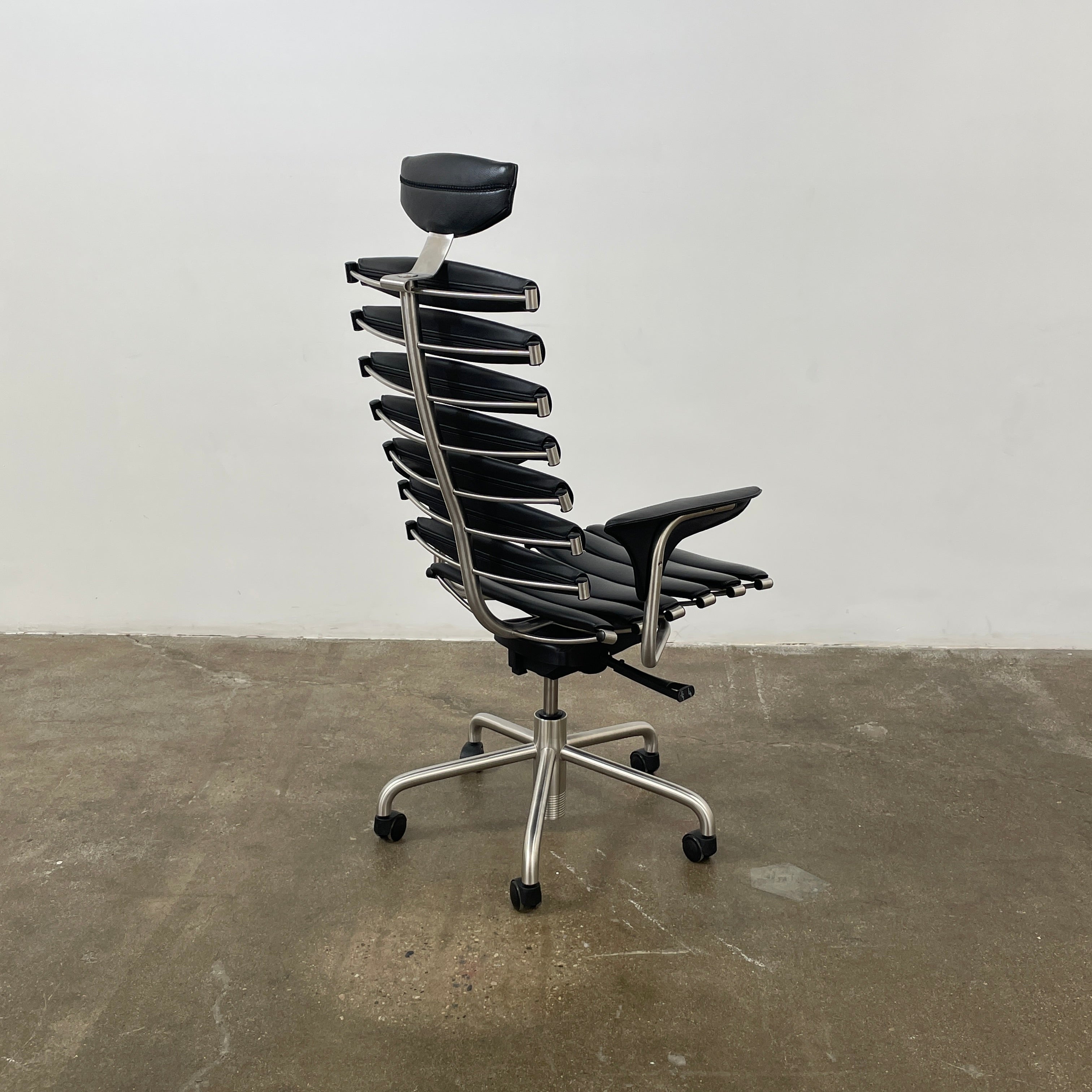The De Sede DS-2100 High-Backed Executive Office Chair features a segmented black leather backrest, adjustable armrests, headrest, and a sturdy metal swivel base with five caster wheels.