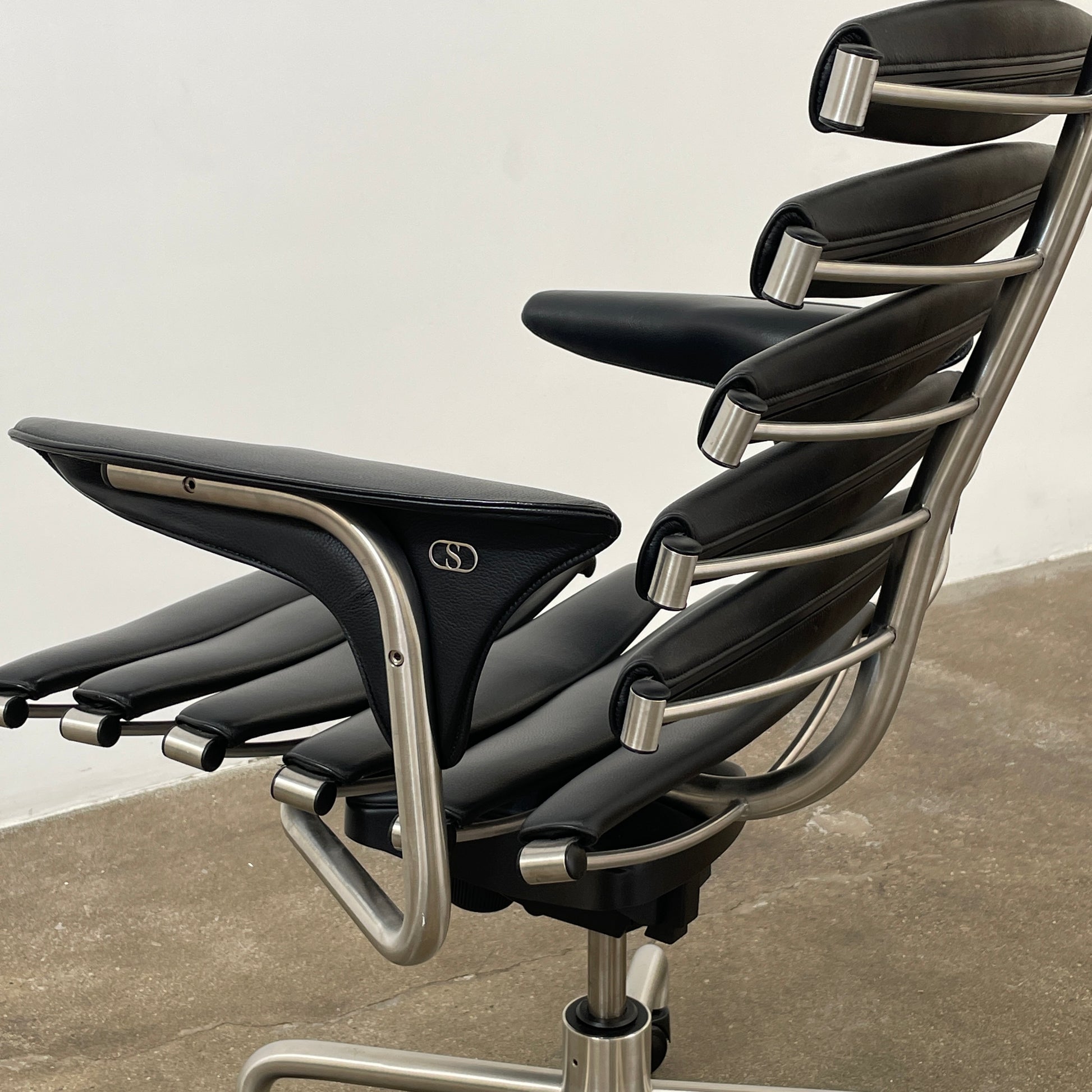 The De Sede DS-2100 High-Backed Executive Office Chair features a segmented black leather backrest, adjustable armrests, headrest, and a sturdy metal swivel base with five caster wheels.