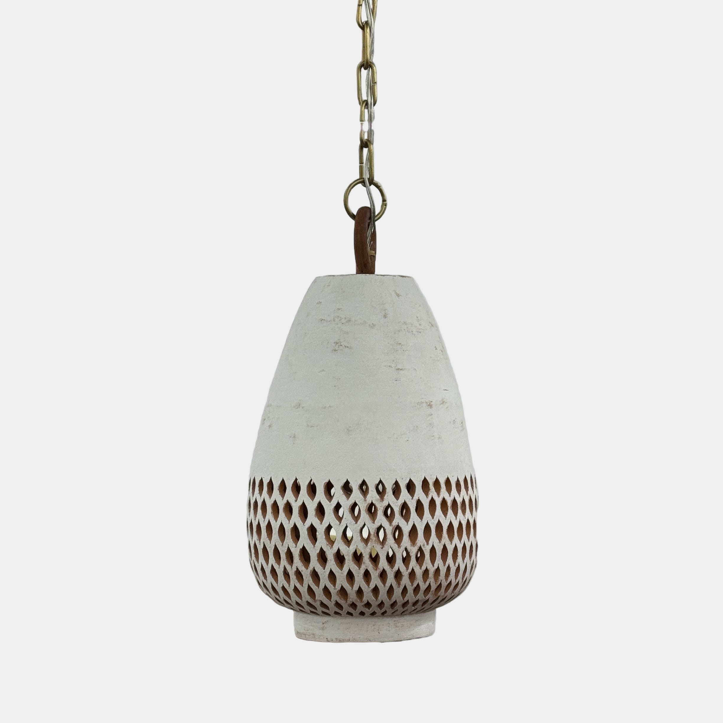 The L’aviva Diamantes Pendant Light, Size B by L’aviva features a white ceramic shade with hand-cut clay patterns, inspired by Oaxacan pottery, and hangs in a modern room with art and contemporary furniture.