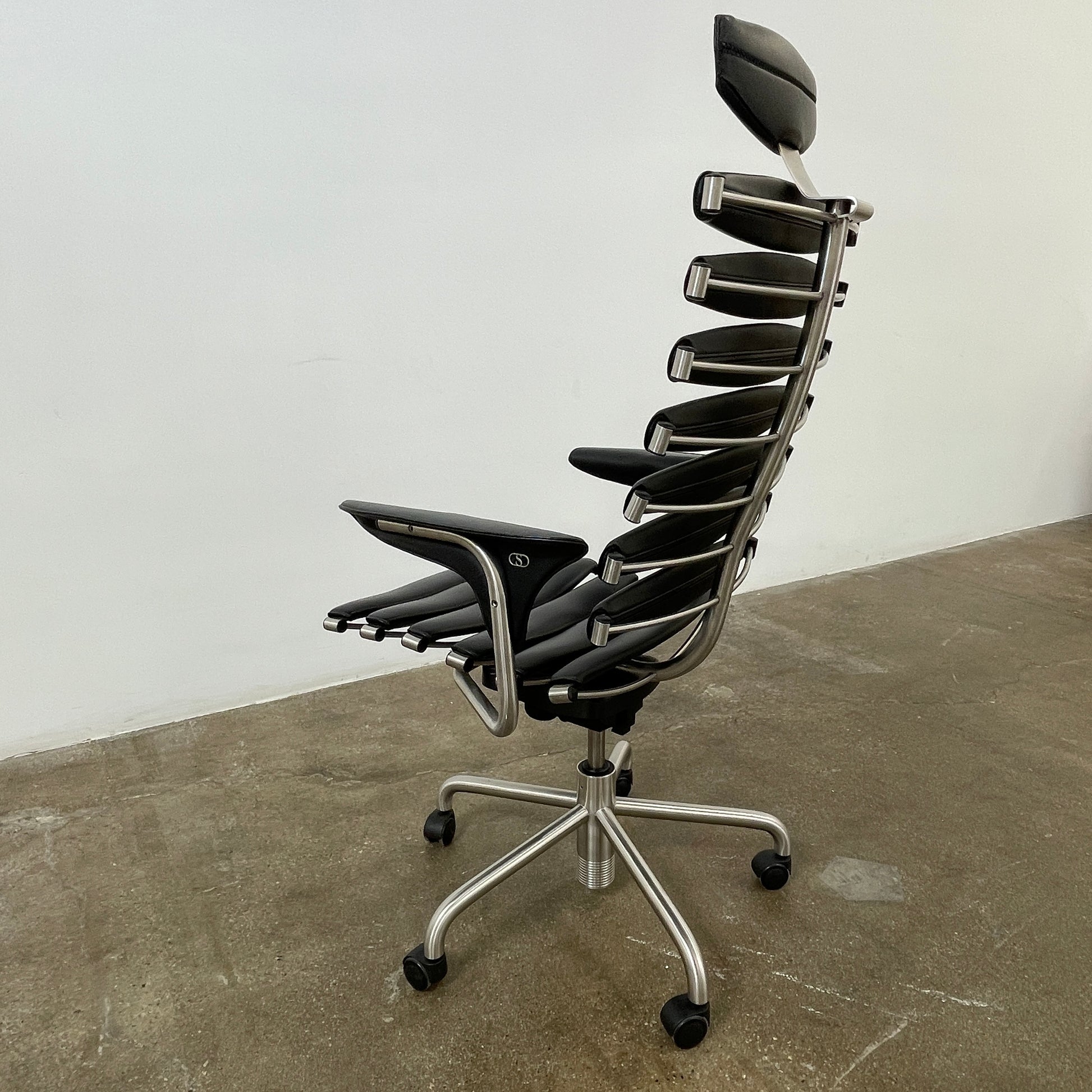 The De Sede DS-2100 High-Backed Executive Office Chair features a segmented black leather backrest, adjustable armrests, headrest, and a sturdy metal swivel base with five caster wheels.