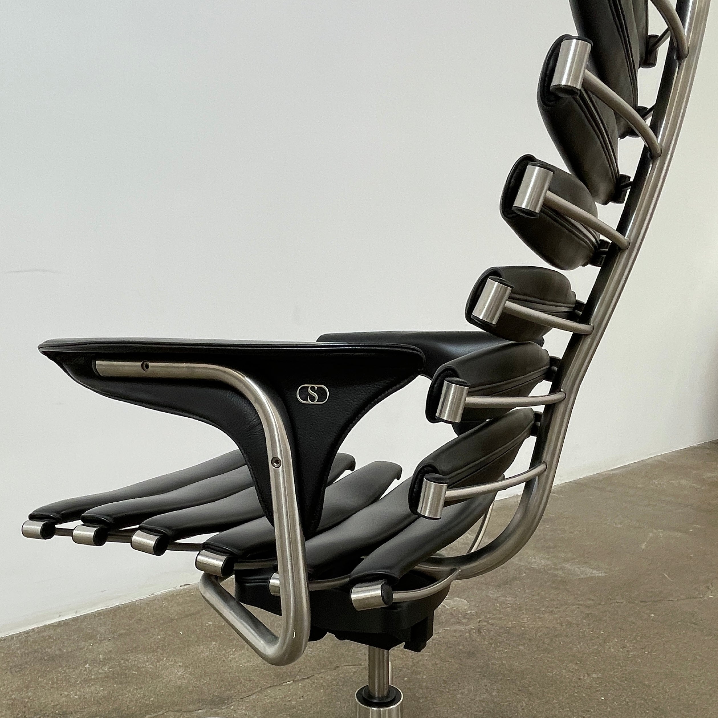 The De Sede DS-2100 High-Backed Executive Office Chair features a segmented black leather backrest, adjustable armrests, headrest, and a sturdy metal swivel base with five caster wheels.