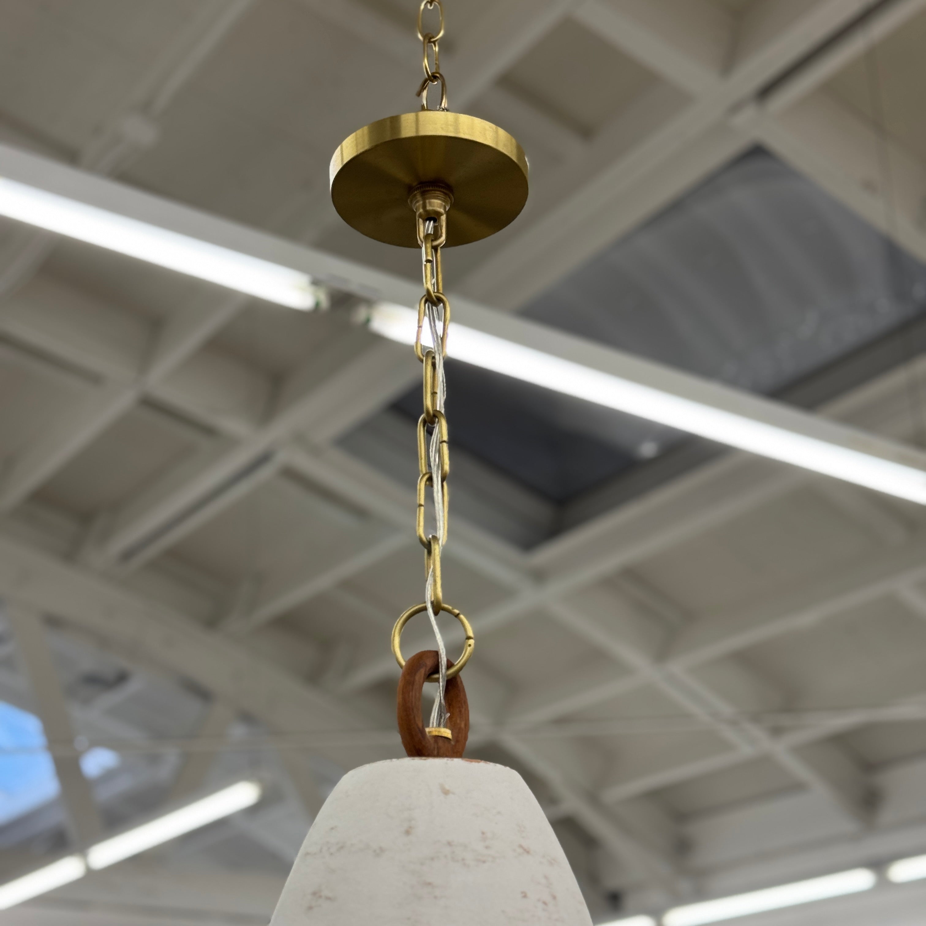 The L’aviva Diamantes Pendant Light, Size B by L’aviva features a white ceramic shade with hand-cut clay patterns, inspired by Oaxacan pottery, and hangs in a modern room with art and contemporary furniture.