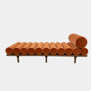 The Tacchini Five to Nine Day Bed by Tacchini features orange cylindrical cushions on a wooden frame—an ideal modern piece for an artist studio, shown here against a plain white background.