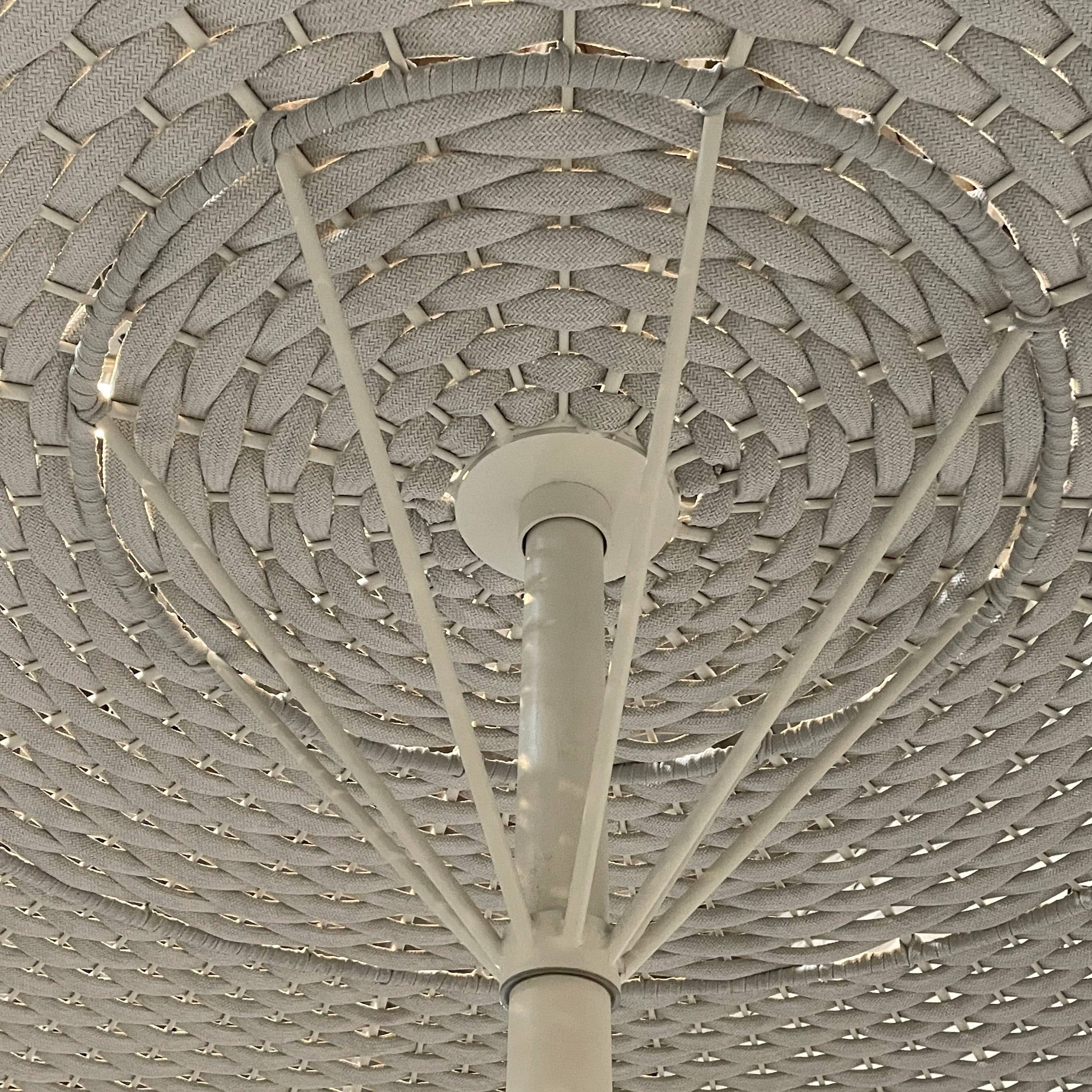 A Paola Lenti Mogambo Parasol on a white stand, designed by Paola Lenti.