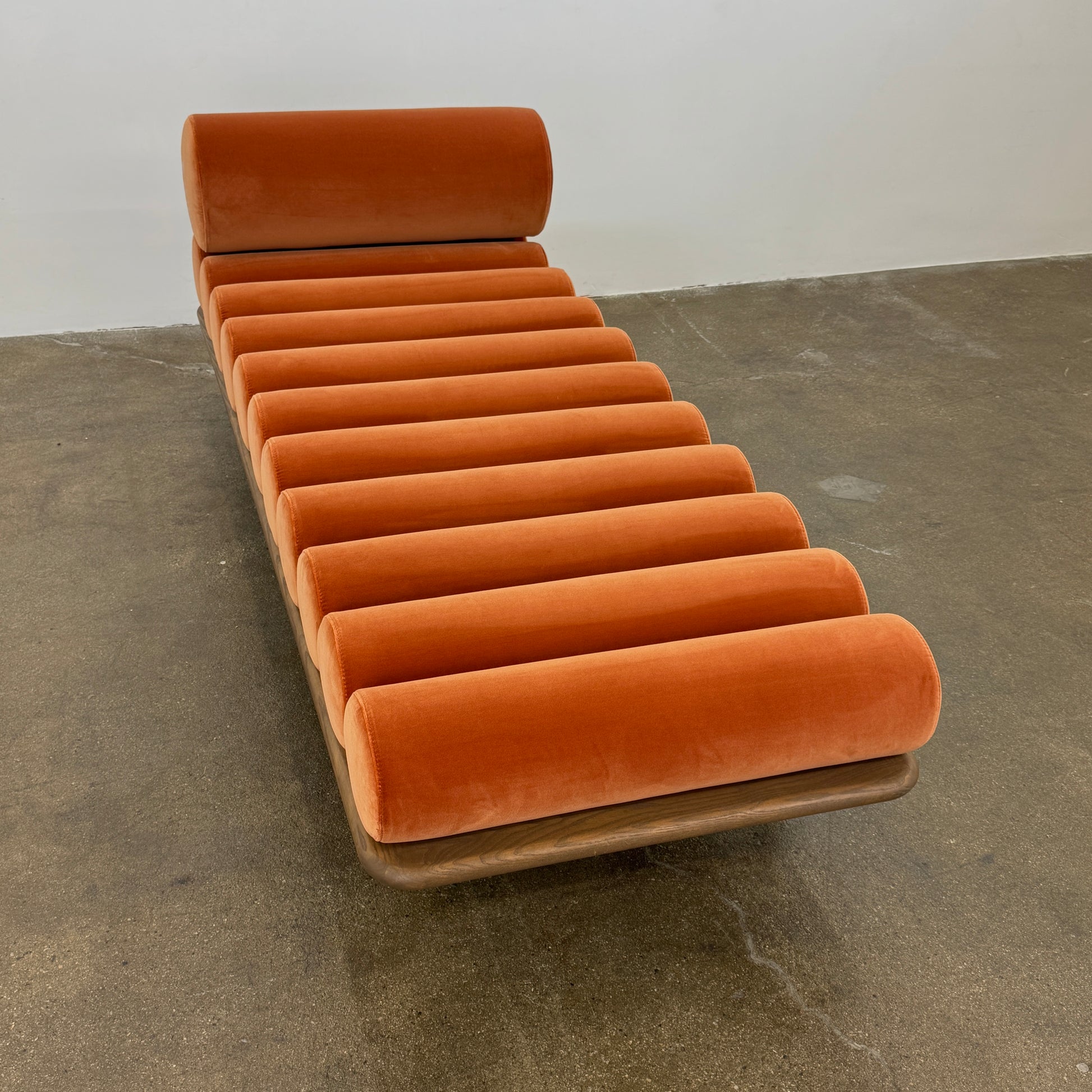 The Tacchini Five to Nine Day Bed by Tacchini features orange cylindrical cushions on a wooden frame—an ideal modern piece for an artist studio, shown here against a plain white background.