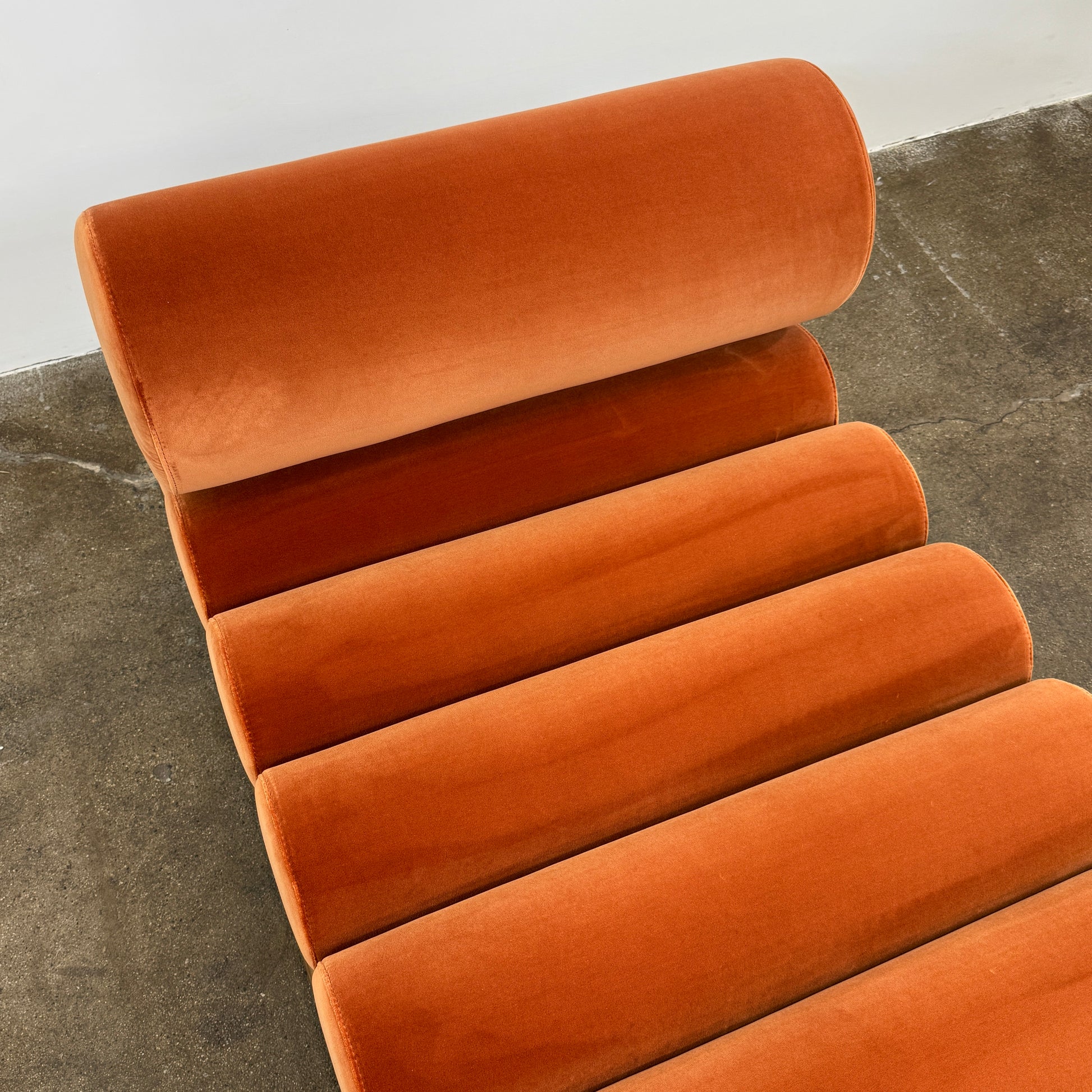 The Tacchini Five to Nine Day Bed by Tacchini features orange cylindrical cushions on a wooden frame—an ideal modern piece for an artist studio, shown here against a plain white background.