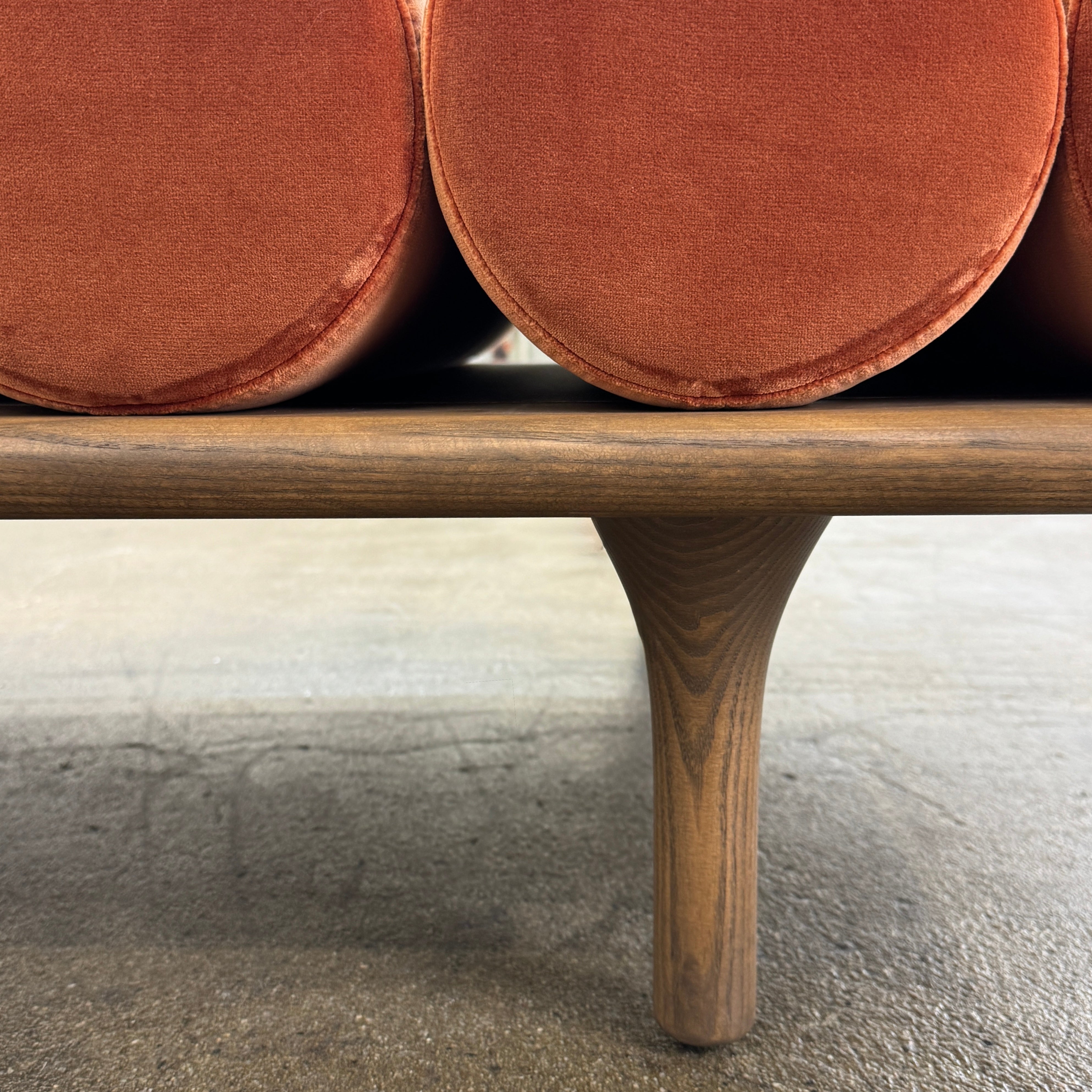 The Tacchini Five to Nine Day Bed by Tacchini features orange cylindrical cushions on a wooden frame—an ideal modern piece for an artist studio, shown here against a plain white background.