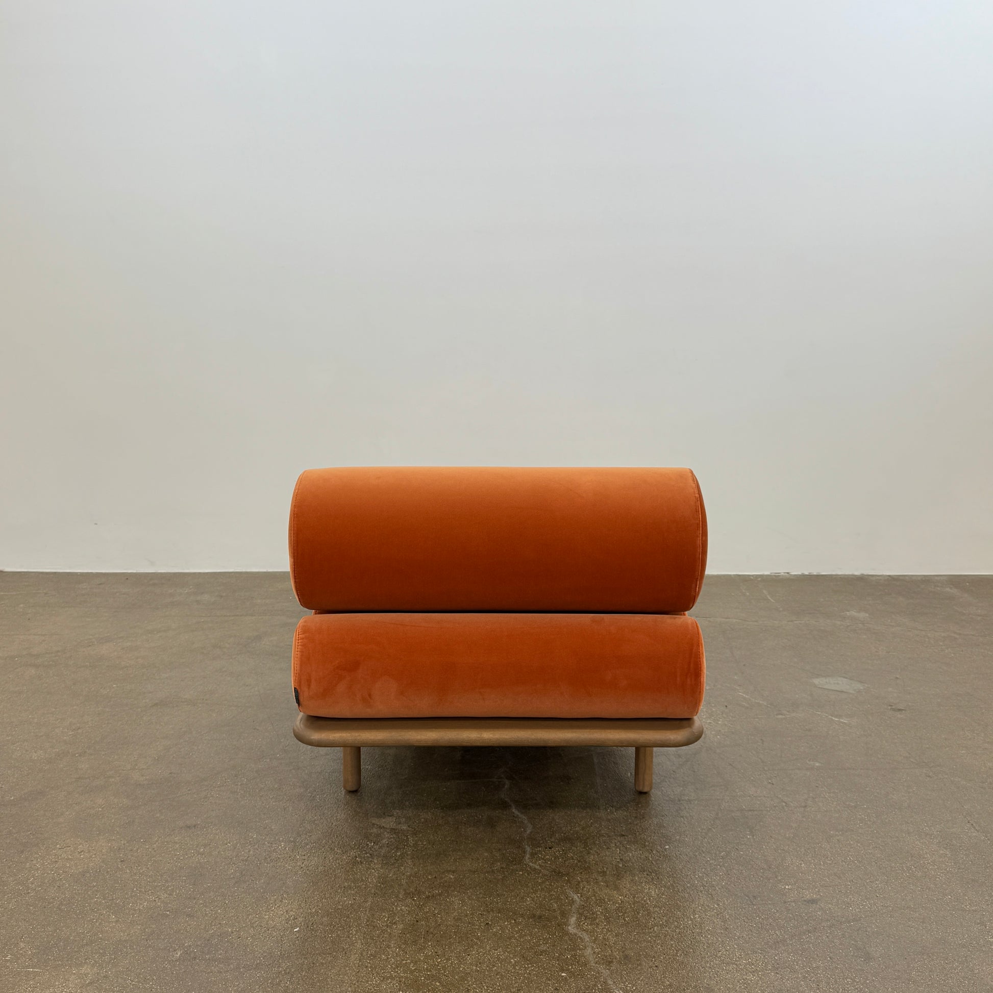 The Tacchini Five to Nine Day Bed by Tacchini features orange cylindrical cushions on a wooden frame—an ideal modern piece for an artist studio, shown here against a plain white background.
