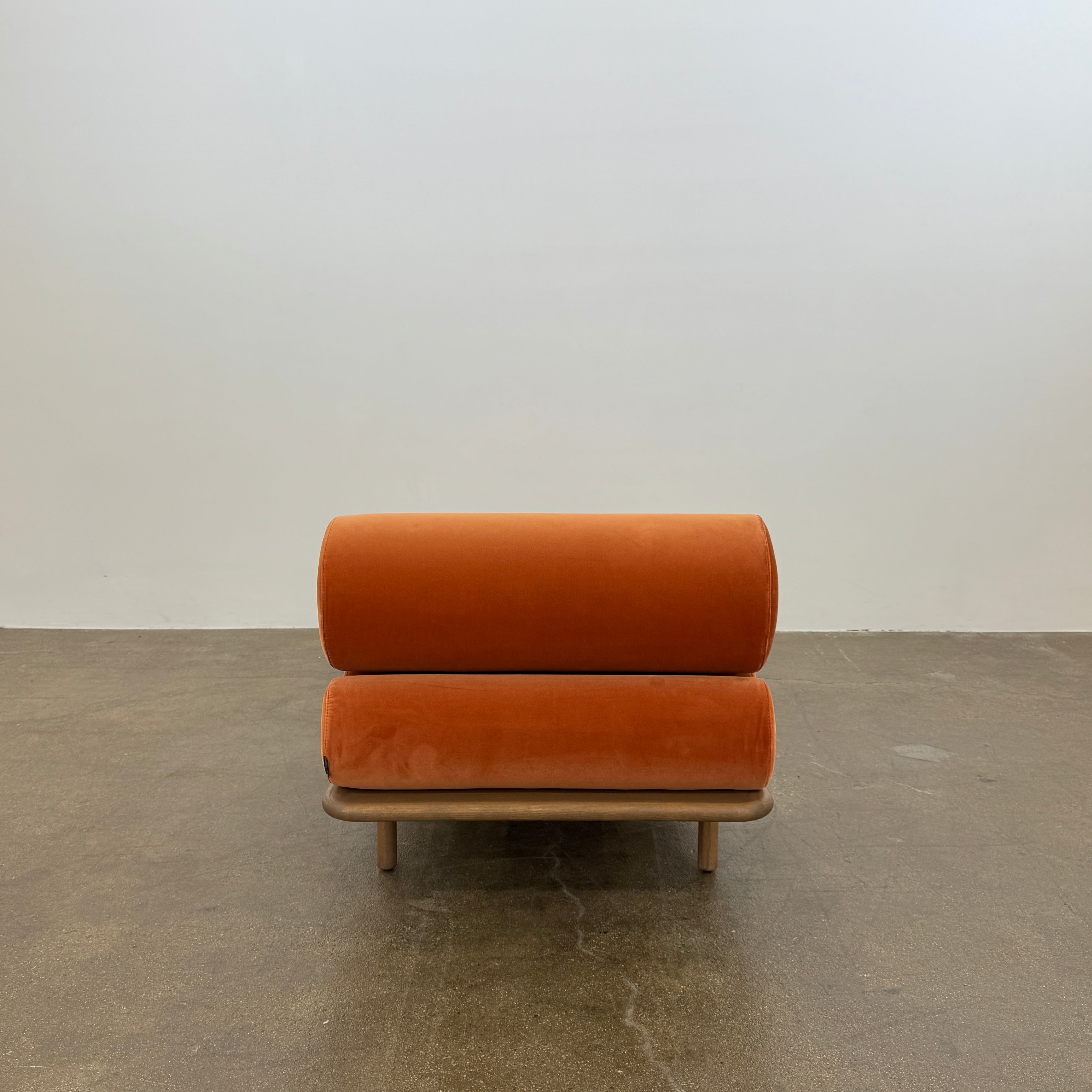 The Tacchini Five to Nine Day Bed by Tacchini features orange cylindrical cushions on a wooden frame—an ideal modern piece for an artist studio, shown here against a plain white background.