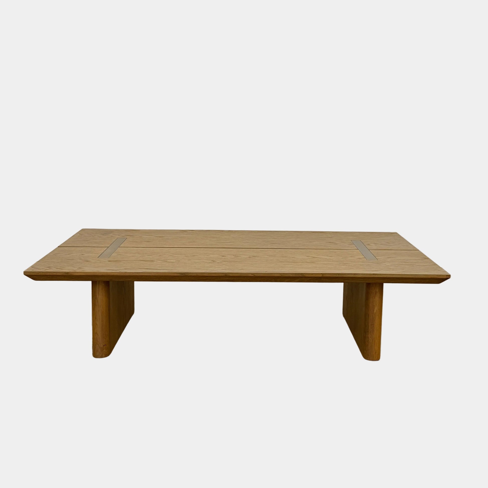 The Harbour Rozzell Coffee Table by Harbour features a rectangular wooden design with two wide legs, set on a concrete floor beside a plain white wall.