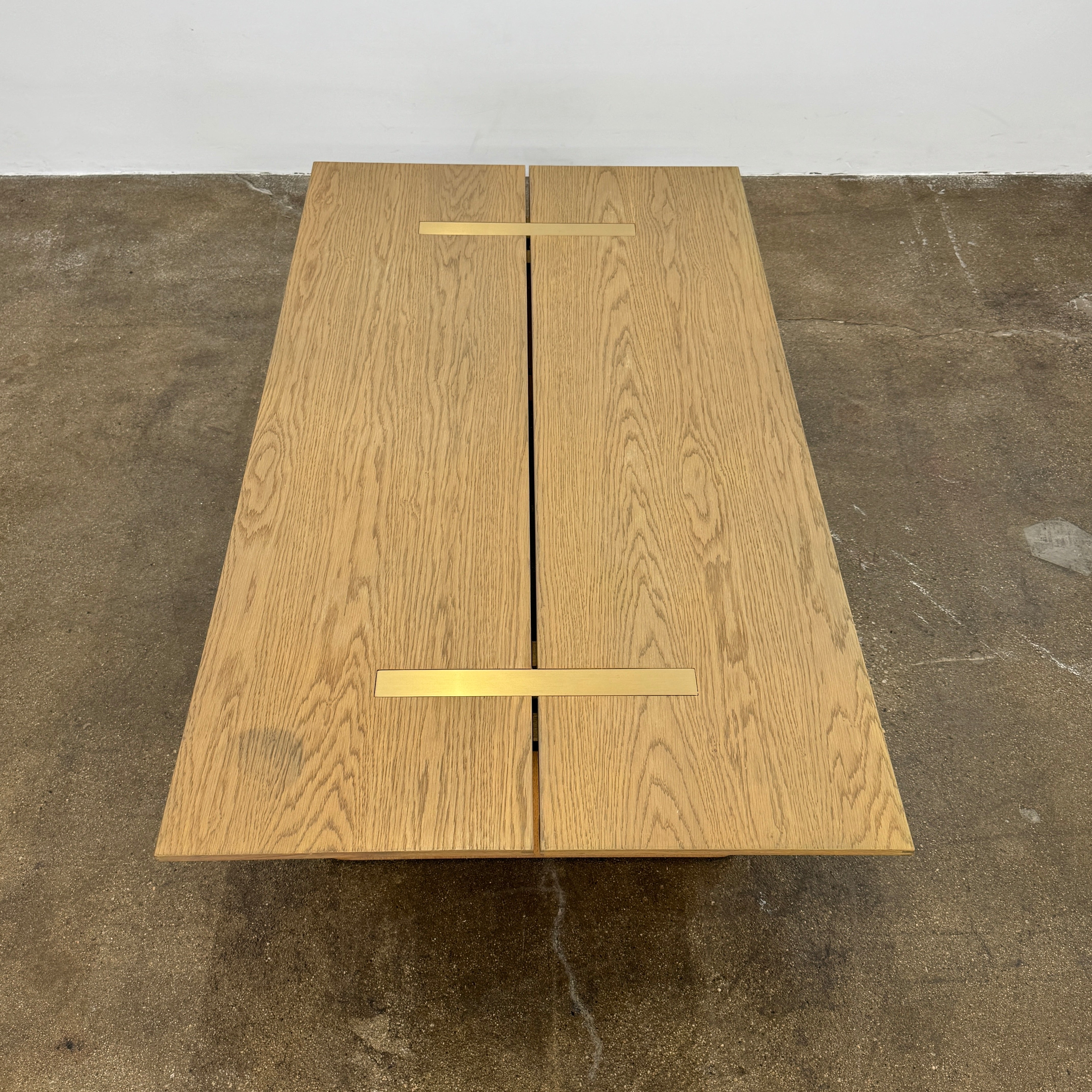 The Harbour Rozzell Coffee Table by Harbour features a rectangular wooden design with two wide legs, set on a concrete floor beside a plain white wall.