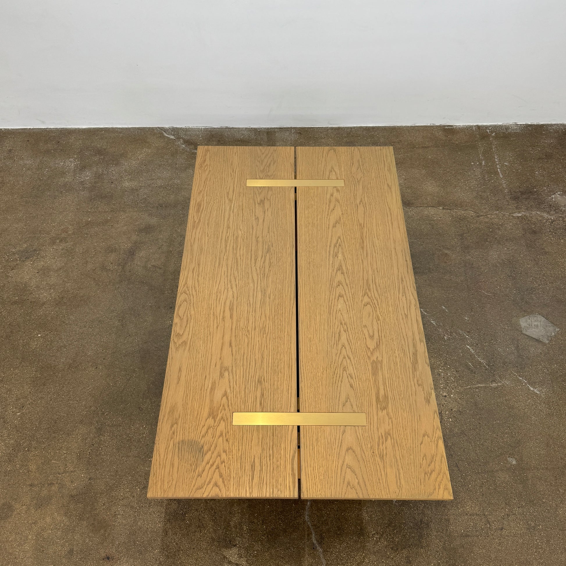 The Harbour Rozzell Coffee Table by Harbour features a rectangular wooden design with two wide legs, set on a concrete floor beside a plain white wall.