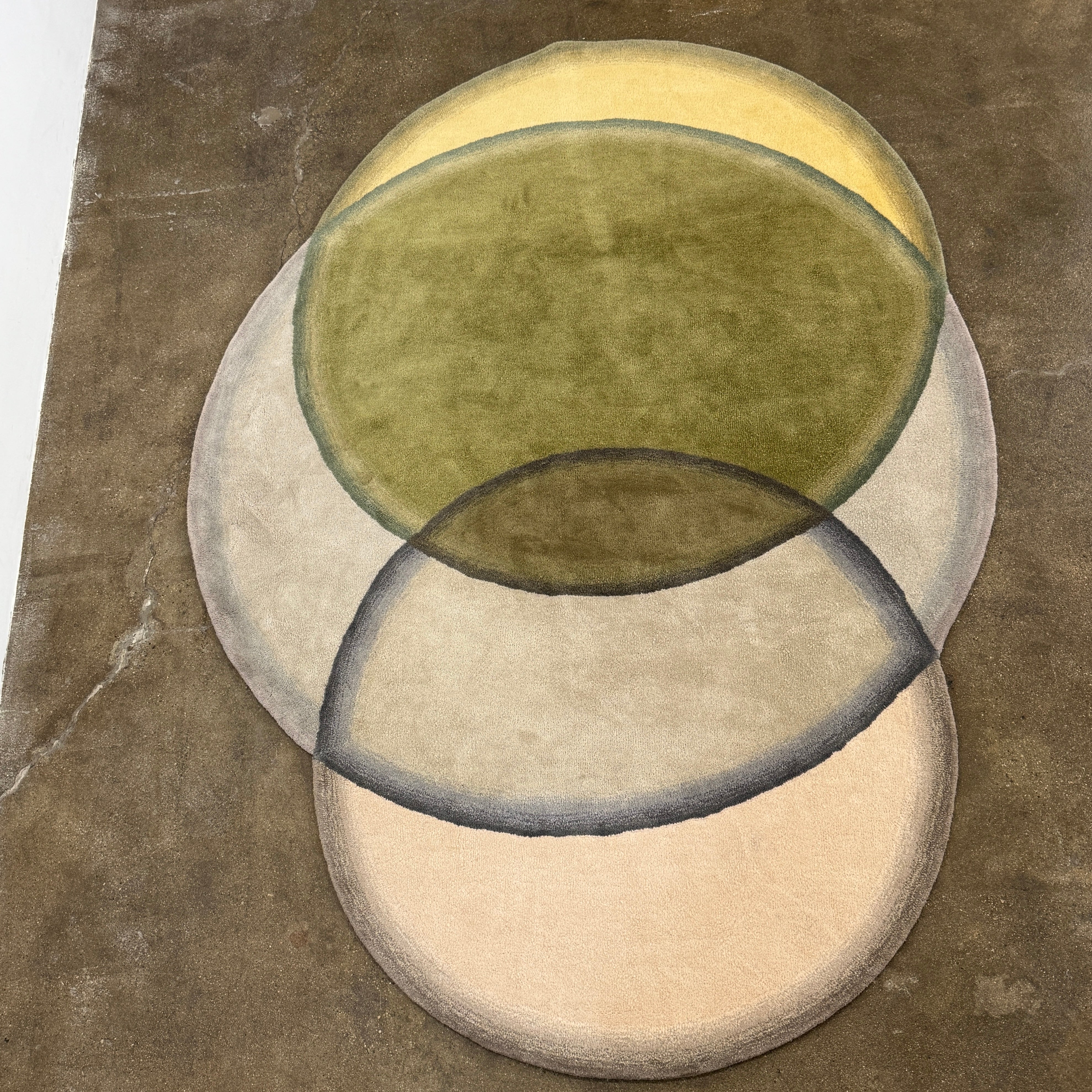 The Gan Crystal Rug by Gan, designed by Charlotte Lancelot, displays three overlapping circles in yellow, green, and beige set against a deep brown background.