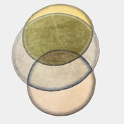 The Gan Crystal Rug by Gan, designed by Charlotte Lancelot, displays three overlapping circles in yellow, green, and beige set against a deep brown background.