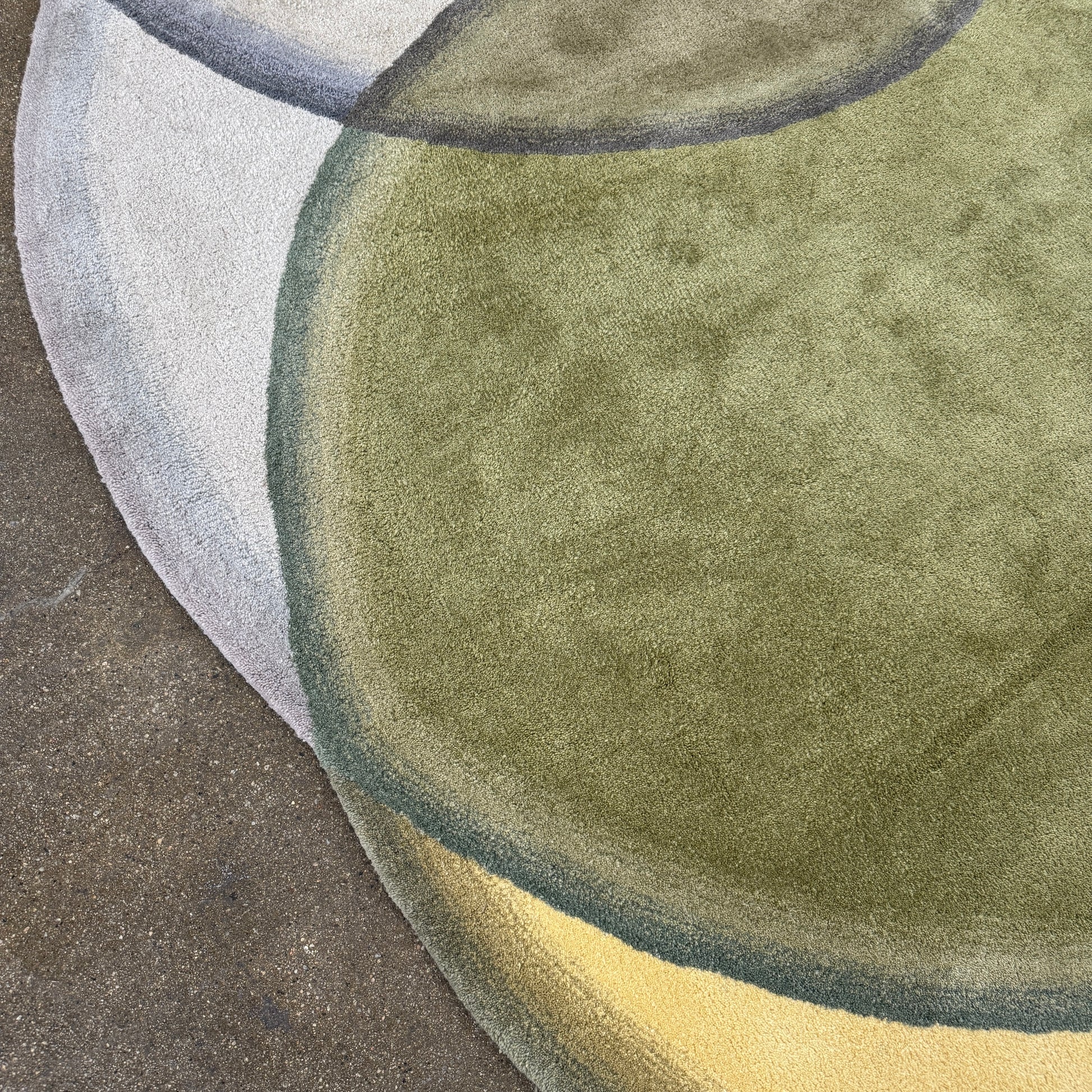 The Gan Crystal Rug by Gan, designed by Charlotte Lancelot, displays three overlapping circles in yellow, green, and beige set against a deep brown background.