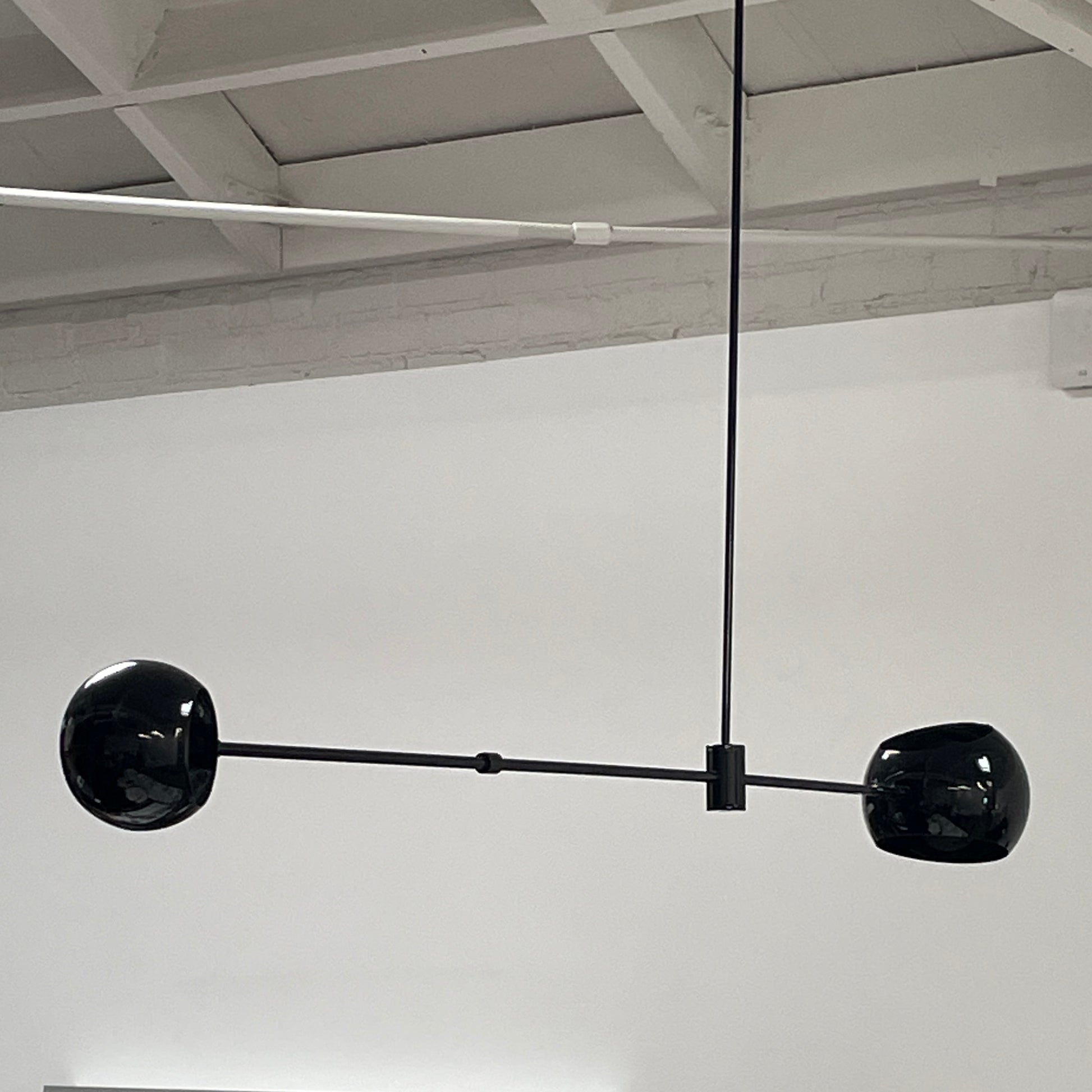 The David Weeks Studio Abaca Suspension Light is a custom-made, black, modern hanging fixture with two spherical bulbs. Crafted from powder-coated steel, it elegantly suspends from ceilings with exposed beams to add sophistication to any space.