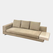 The Minotti White Sofa with Table is a beige three-seater luxury sofa featuring chenille upholstery, wide armrests, three back cushions, and an attached white side table on the right, set against a plain white wall on a brown floor.