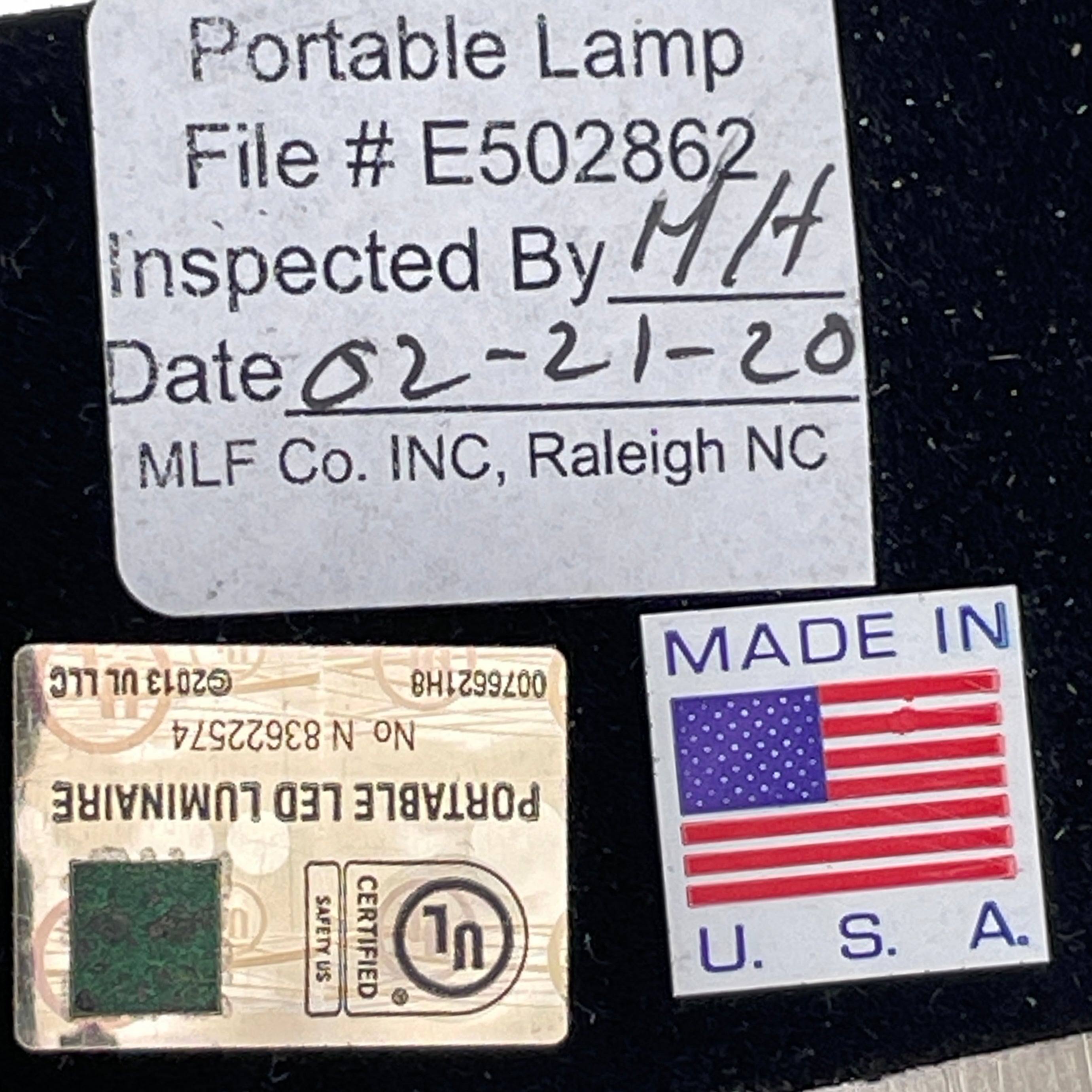 The Holly Hunt Studio Bar Desk Lamp, featuring a modern minimalist design with a rectangular base and adjustable arm, is elegantly placed on a white pedestal against a gray wall.