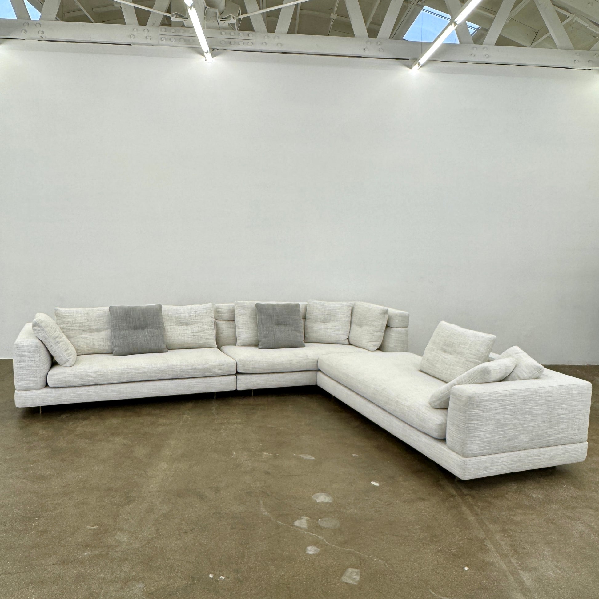 The Minotti Alexander 3 Piece Sectional by Minotti features an L-shaped design in light beige linen blend upholstery with multiple gray and beige throw pillows, set against a plain white background.