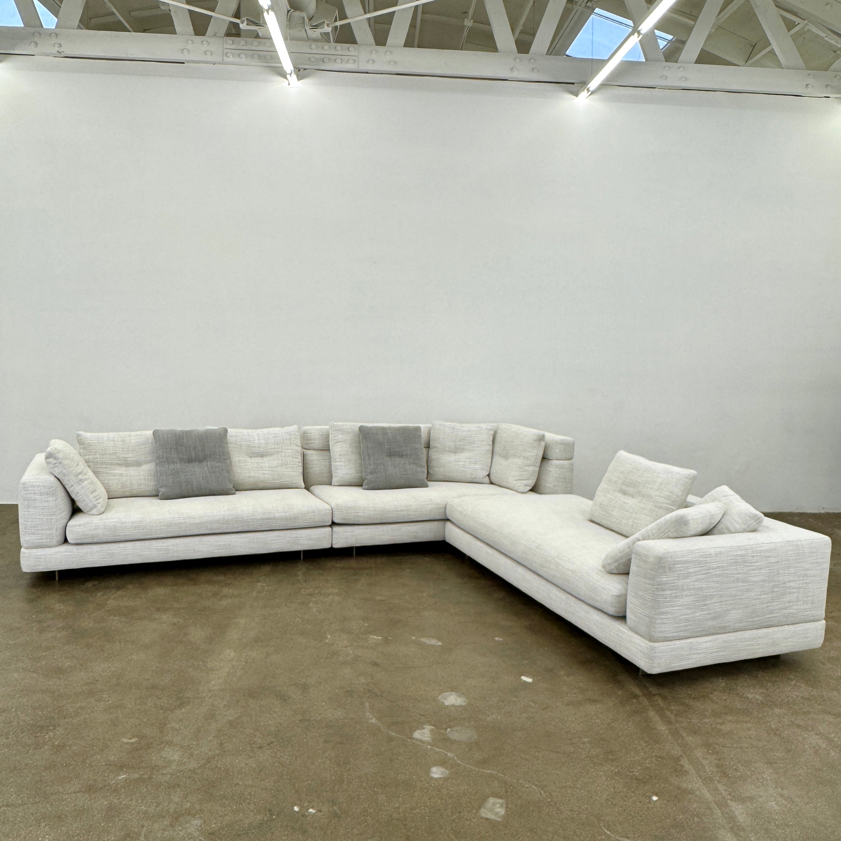 The Minotti Alexander 3 Piece Sectional by Minotti features an L-shaped design in light beige linen blend upholstery with multiple gray and beige throw pillows, set against a plain white background.