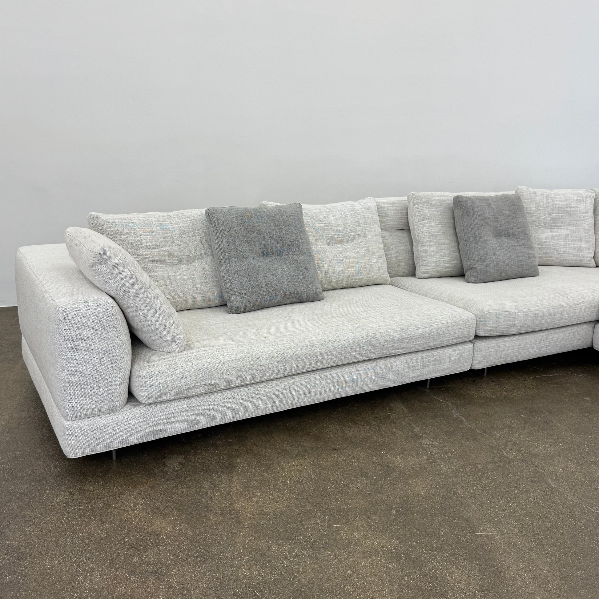 The Minotti Alexander 3 Piece Sectional by Minotti features an L-shaped design in light beige linen blend upholstery with multiple gray and beige throw pillows, set against a plain white background.