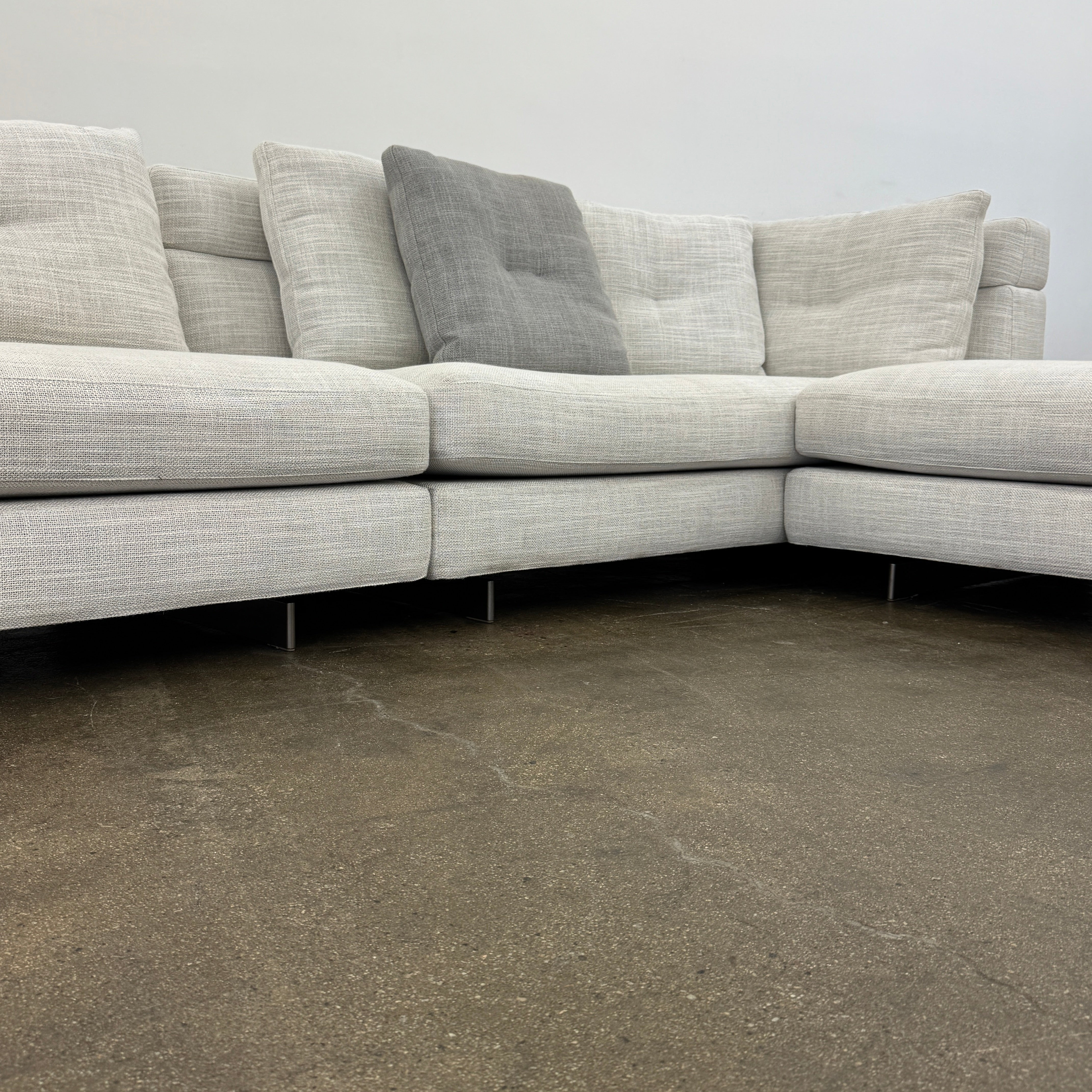 The Minotti Alexander 3 Piece Sectional by Minotti features an L-shaped design in light beige linen blend upholstery with multiple gray and beige throw pillows, set against a plain white background.