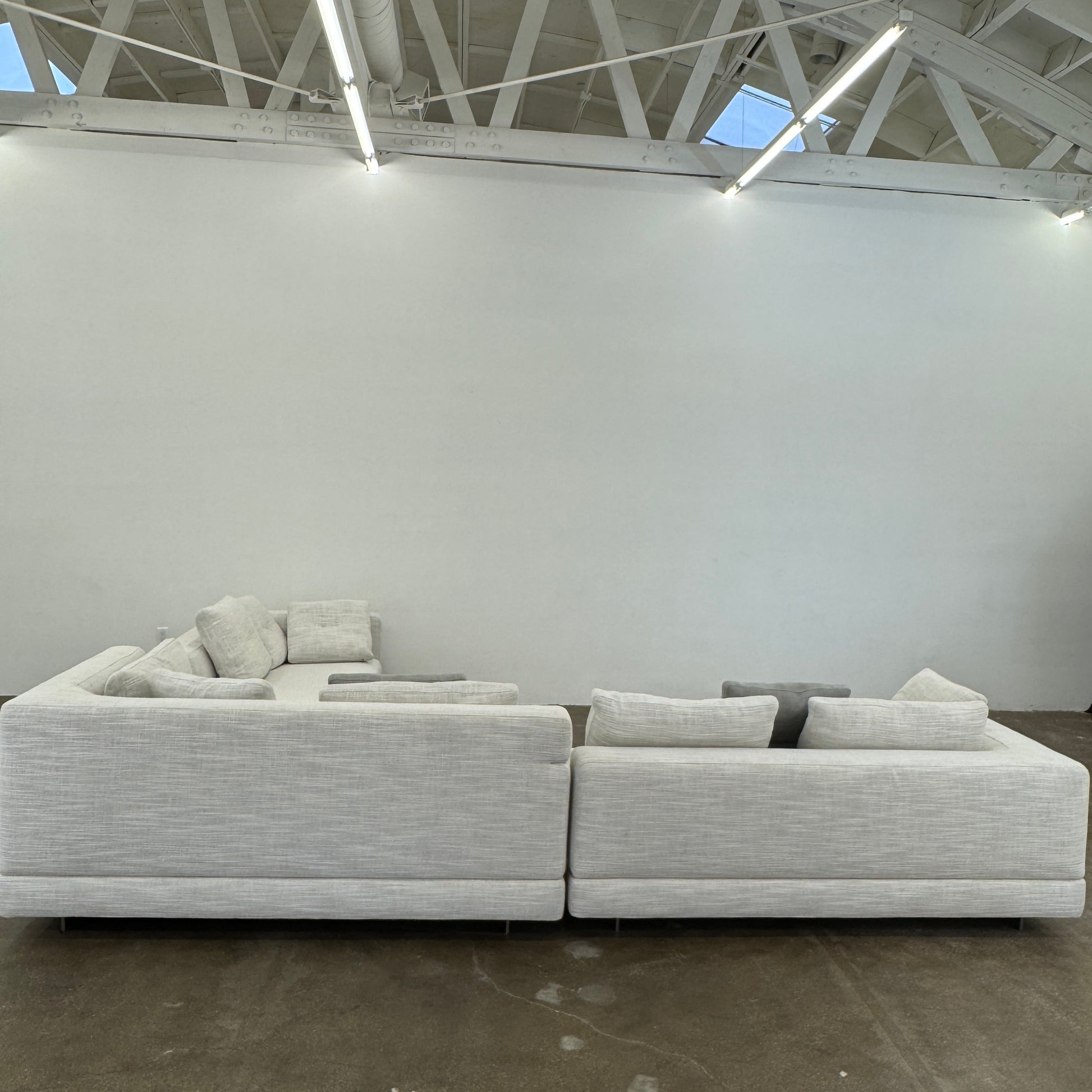 The Minotti Alexander 3 Piece Sectional by Minotti features an L-shaped design in light beige linen blend upholstery with multiple gray and beige throw pillows, set against a plain white background.