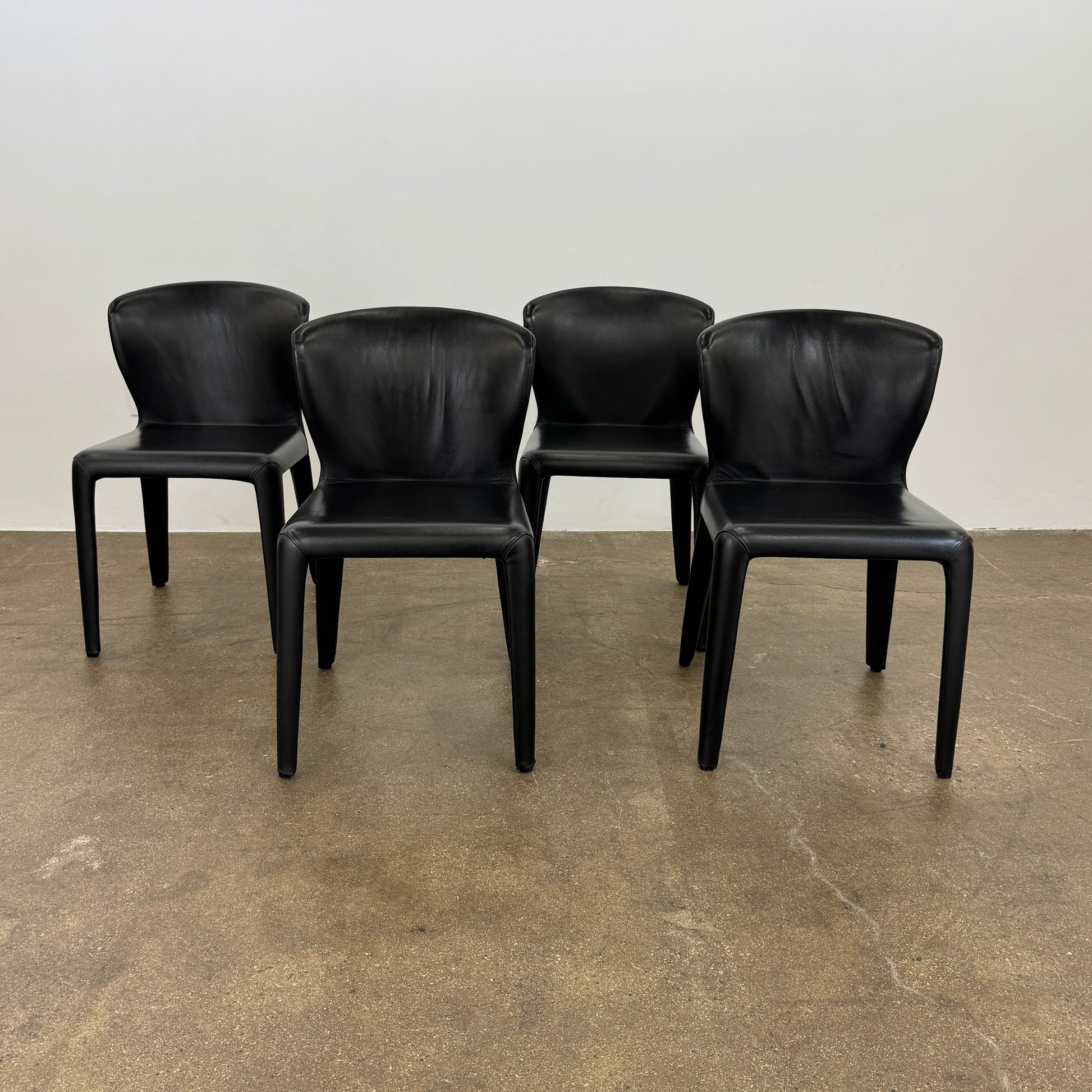 A set of four Cassina Hola Dining Chairs by Cassina, upholstered in black leather, are set in two rows against a plain white background.