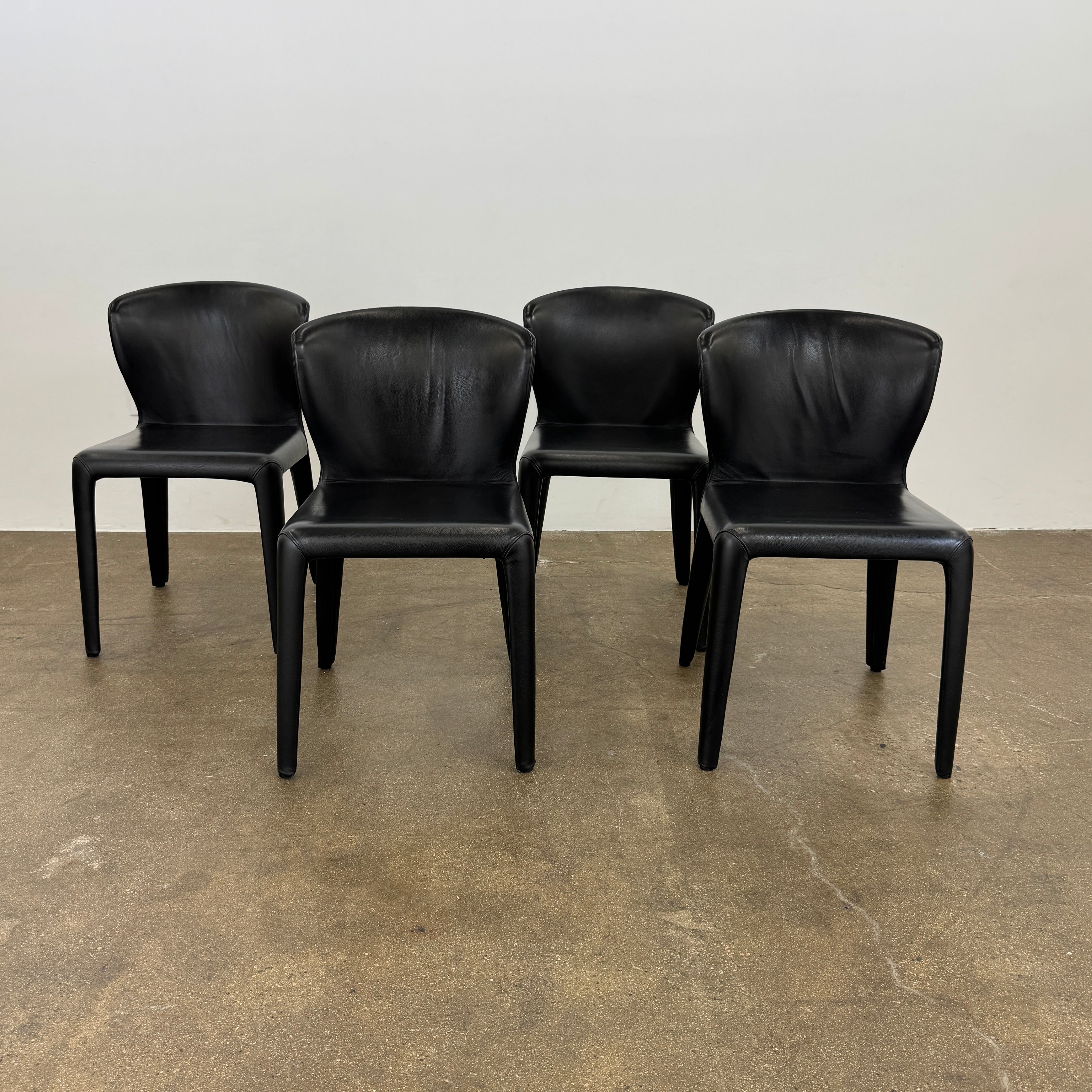 A set of four Cassina Hola Dining Chairs by Cassina, upholstered in black leather, are set in two rows against a plain white background.