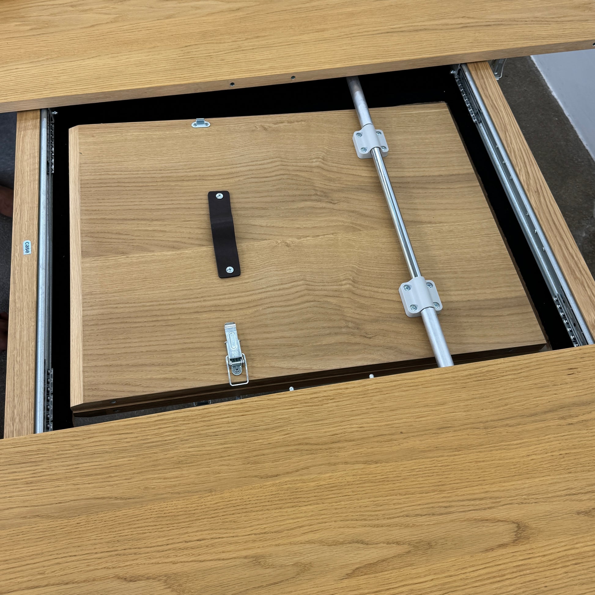 A Case Dulwich Extension Table, round and wooden with four legs, stands on a concrete floor against a plain white wall.