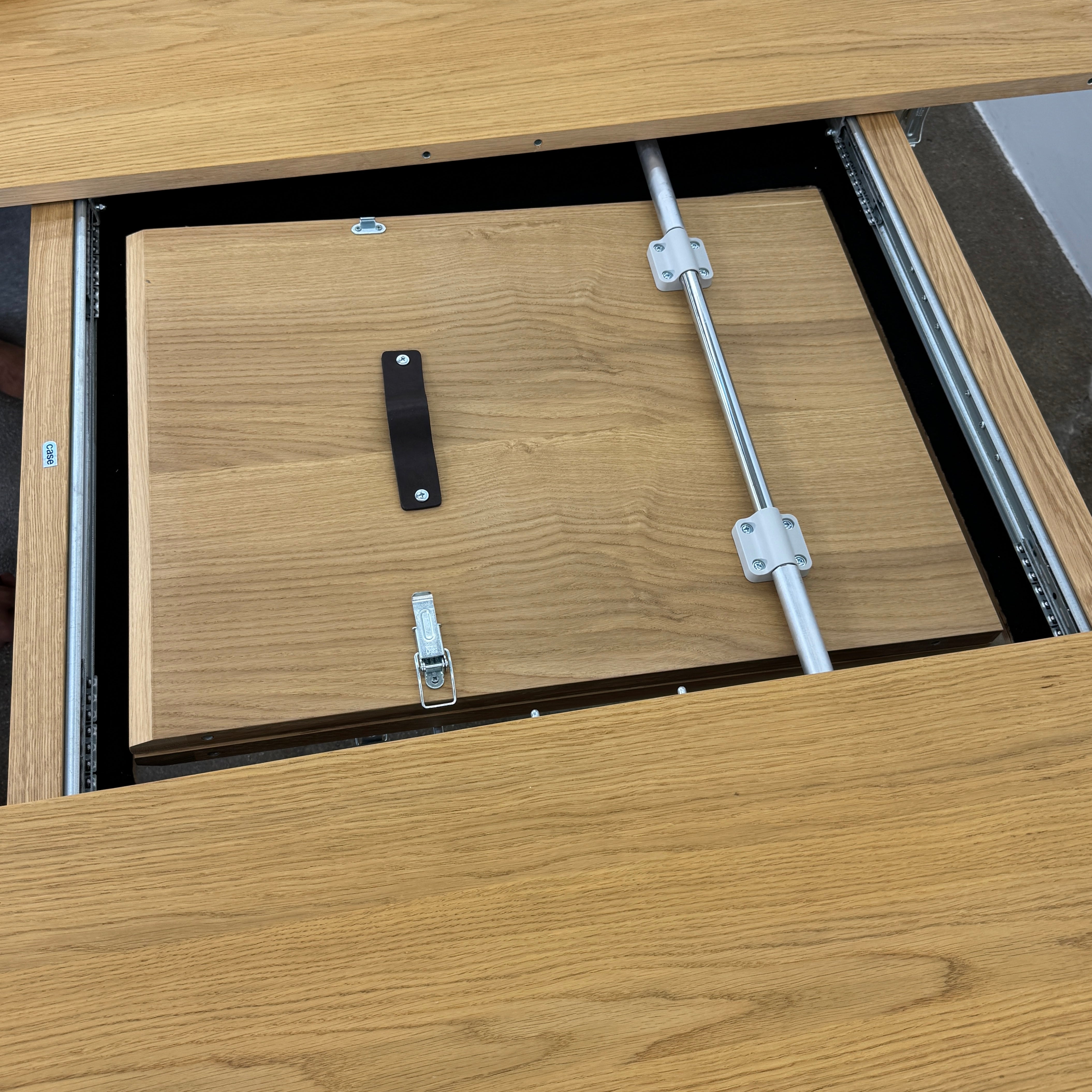 A Case Dulwich Extension Table, round and wooden with four legs, stands on a concrete floor against a plain white wall.