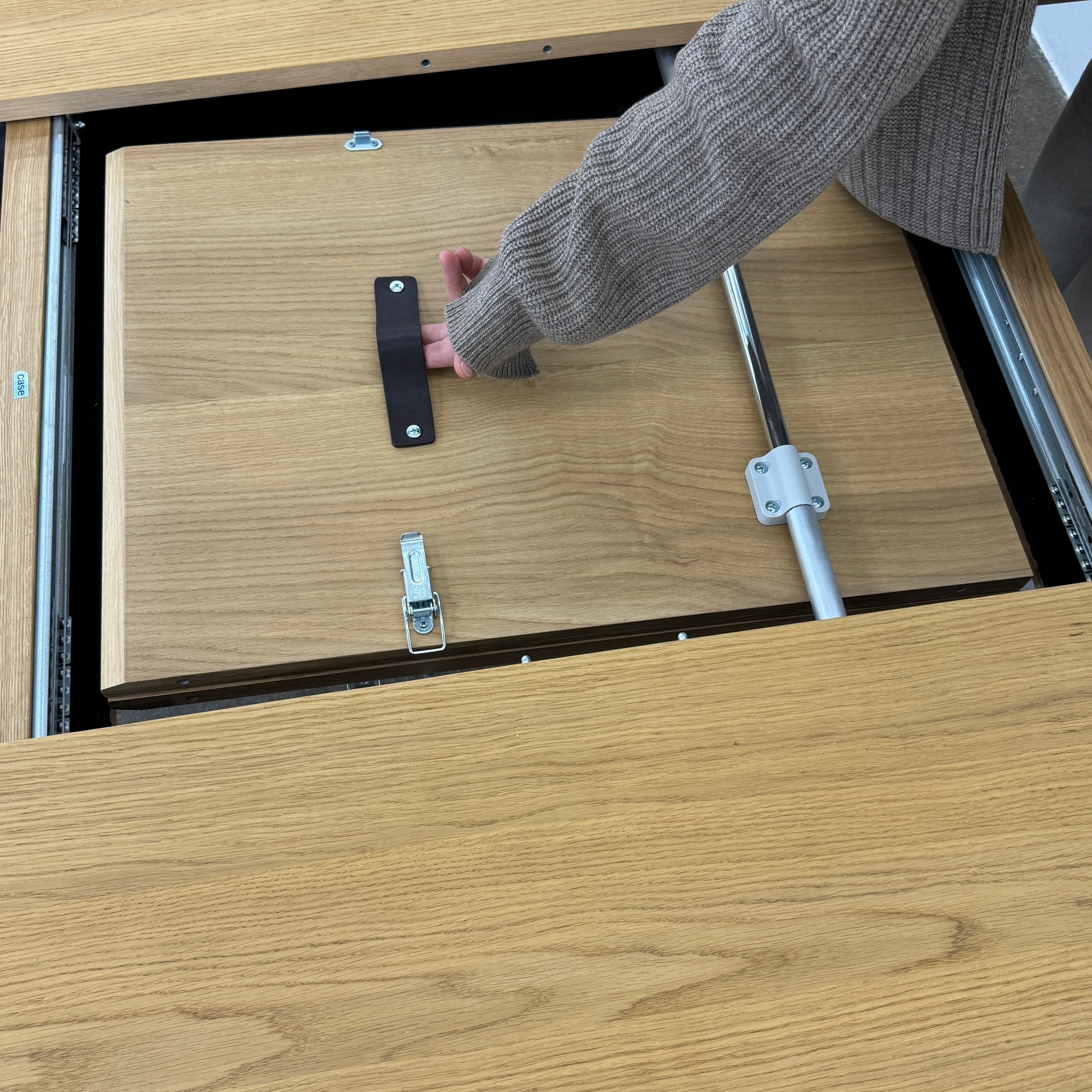 A Case Dulwich Extension Table, round and wooden with four legs, stands on a concrete floor against a plain white wall.