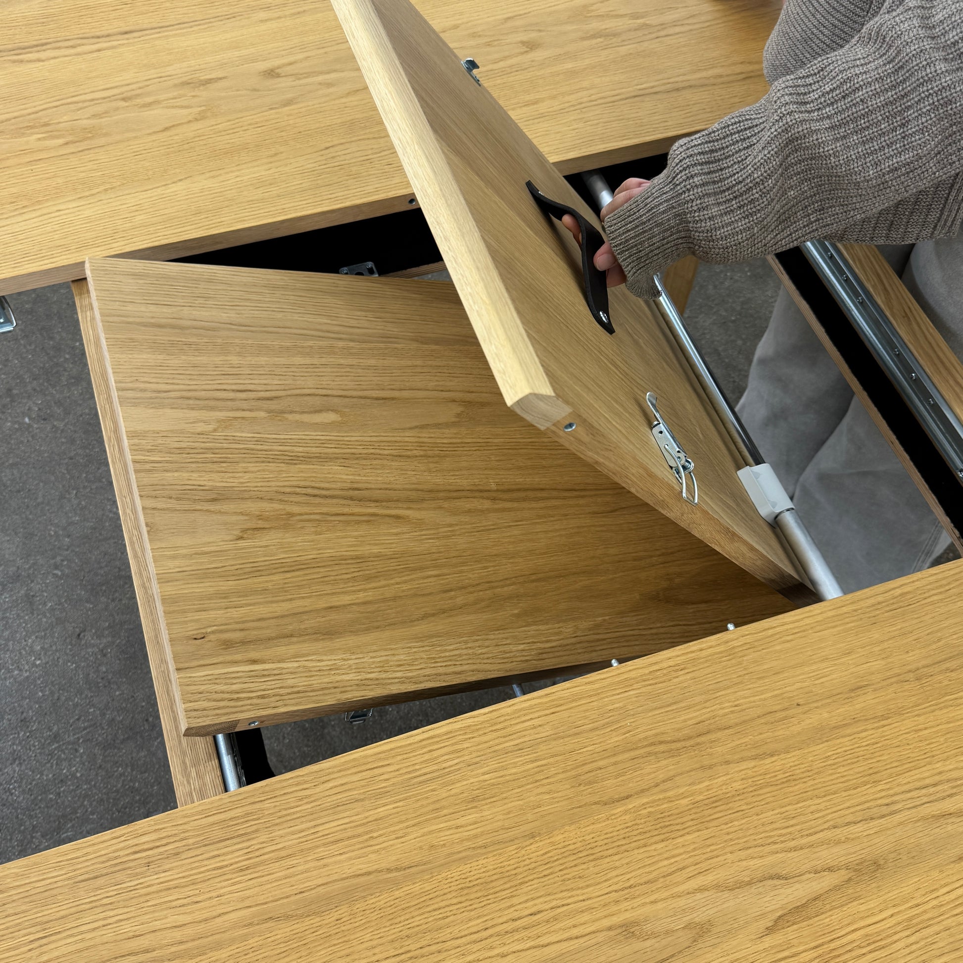 A Case Dulwich Extension Table, round and wooden with four legs, stands on a concrete floor against a plain white wall.