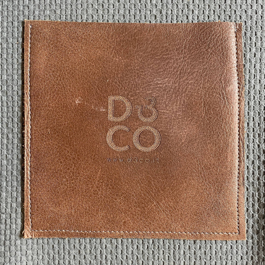 A unique brown leather pouch with the word D3CO on it, featuring a modern Italian design.