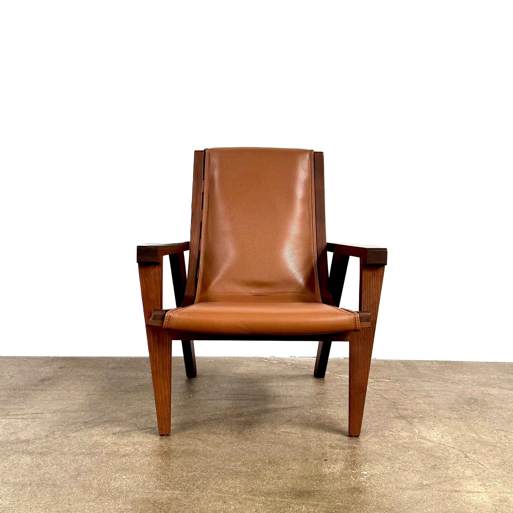 A contemporary B&B Italia JJ Armchair with brown leather seat and backrest, angular armrests, and a dark wooden frame, designed by Antonio Citterio. Set against a plain white background.