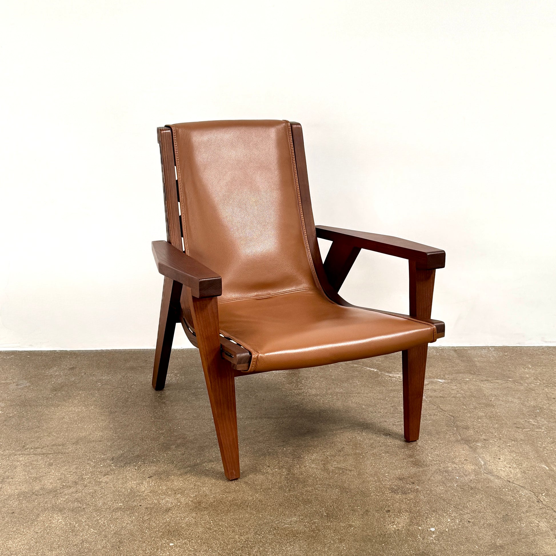 A contemporary B&B Italia JJ Armchair with brown leather seat and backrest, angular armrests, and a dark wooden frame, designed by Antonio Citterio. Set against a plain white background.