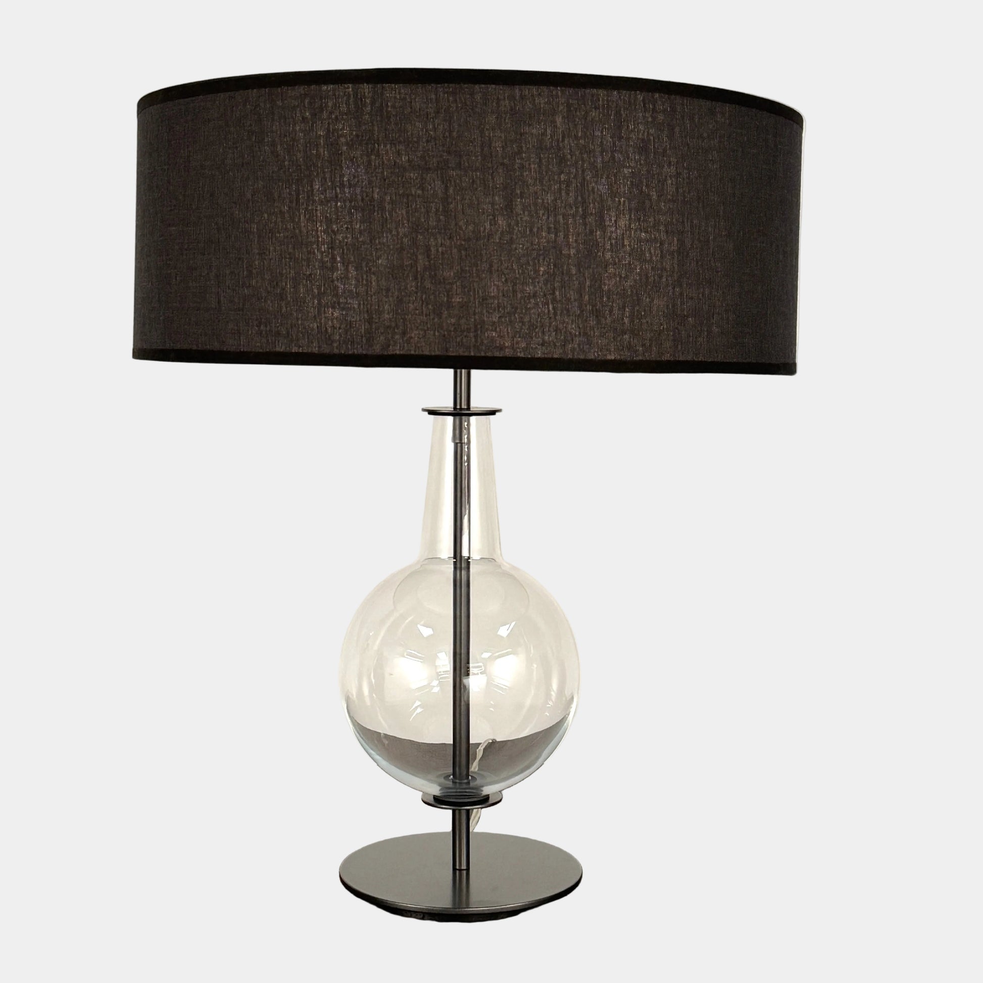 The Penta Classic Desir Table Lamp by Penta features a hand-blown glass base and a large cylindrical black lampshade, showcased against a plain white background.