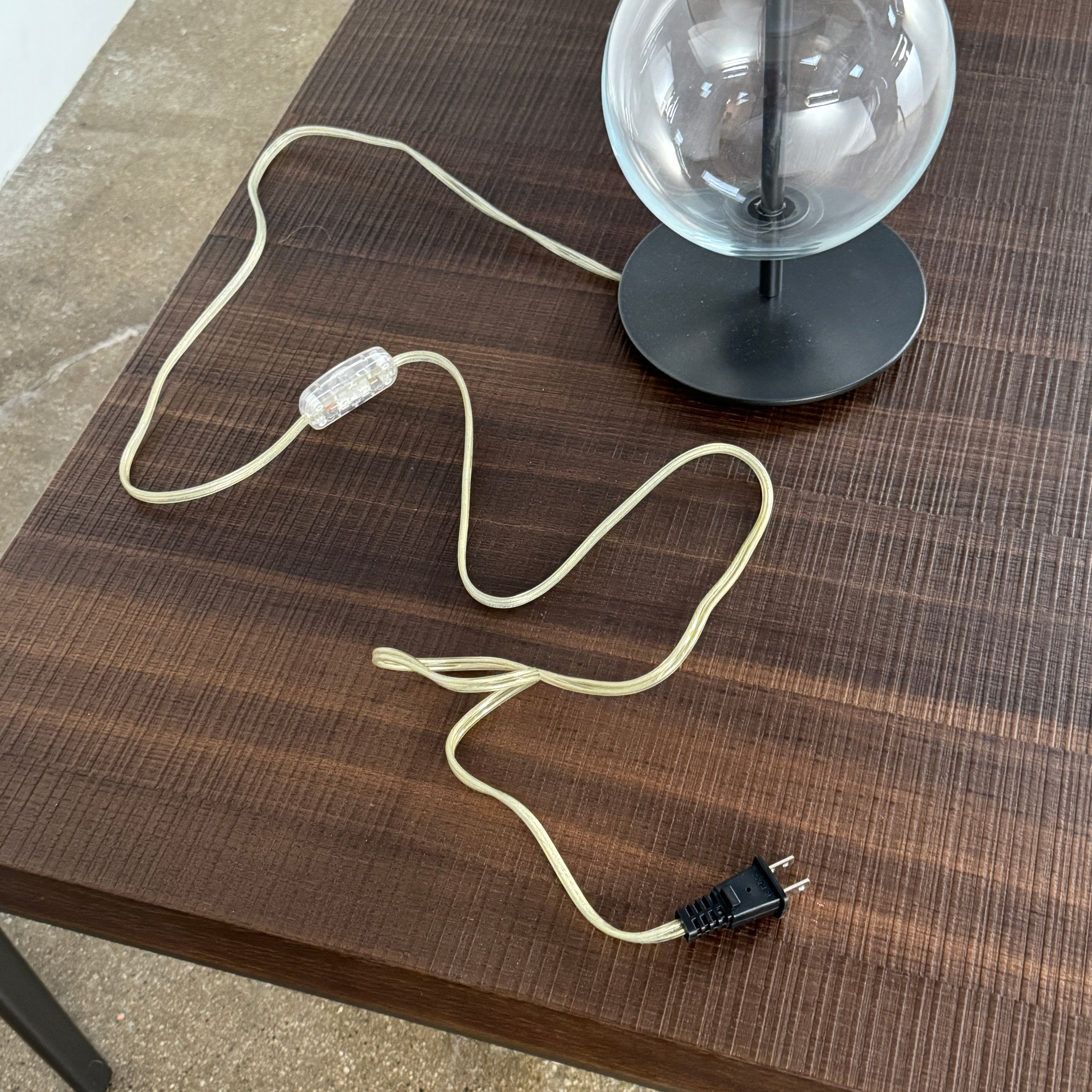 The Penta Classic Desir Table Lamp by Penta features a hand-blown glass base and a large cylindrical black lampshade, showcased against a plain white background.