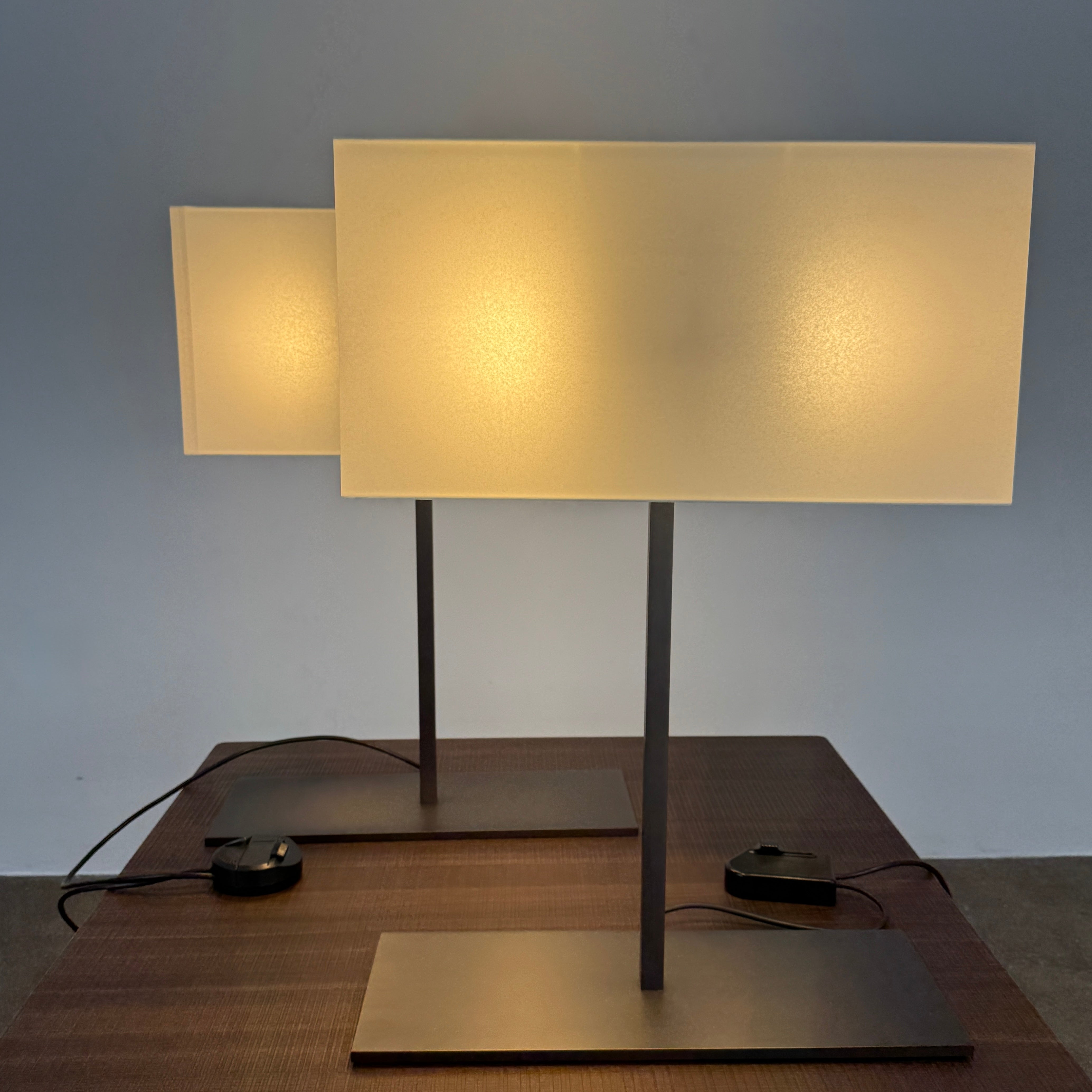 The Maxalto Leukon Table Lamp by Maxalto features a rectangular fabric shade, slim metal stem, and flat base, providing warm, modern lighting.
