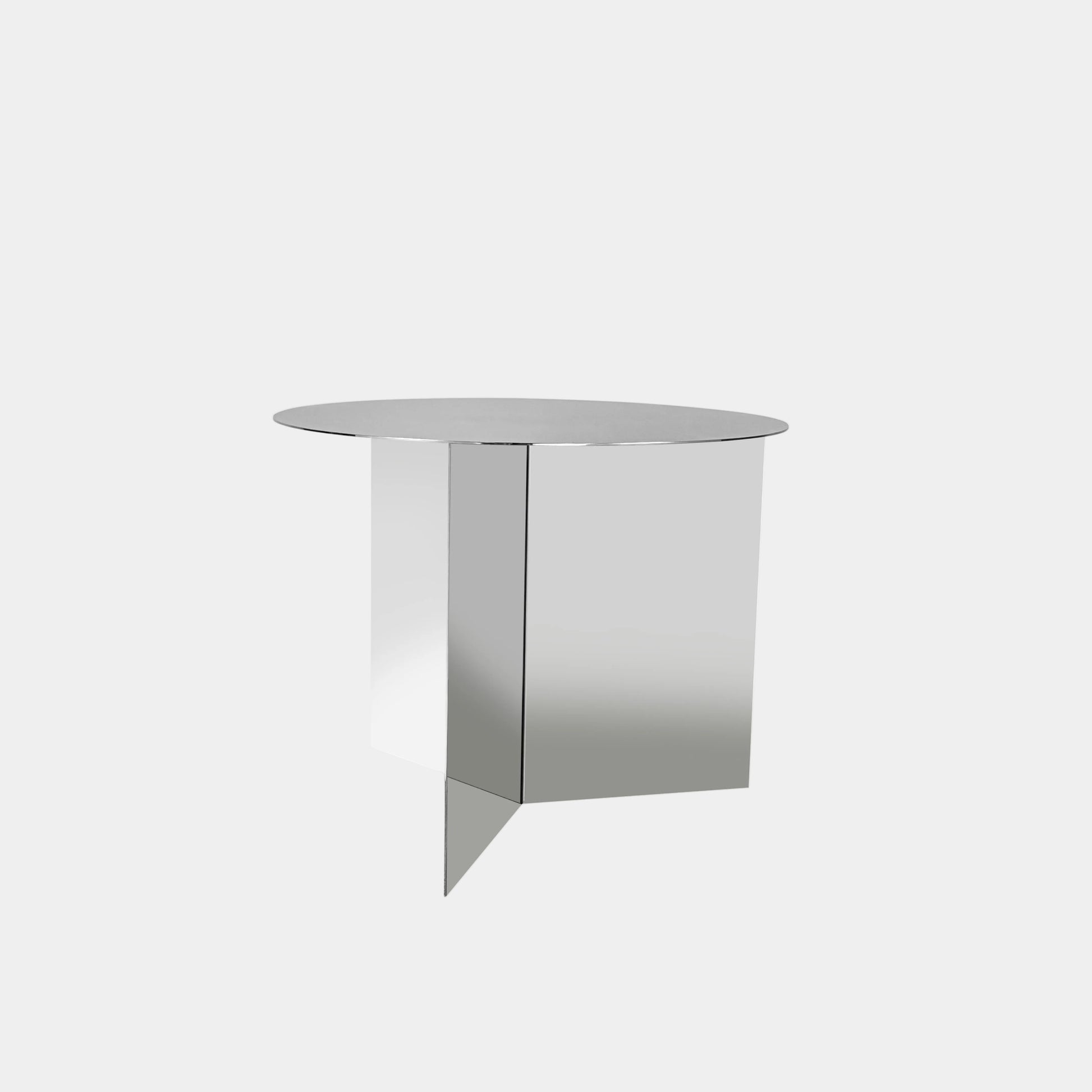 The Hay Slit Side Table by Hay features a round, reflective design with mirrored sides and is shown atop a dark wooden surface against a plain white wall.