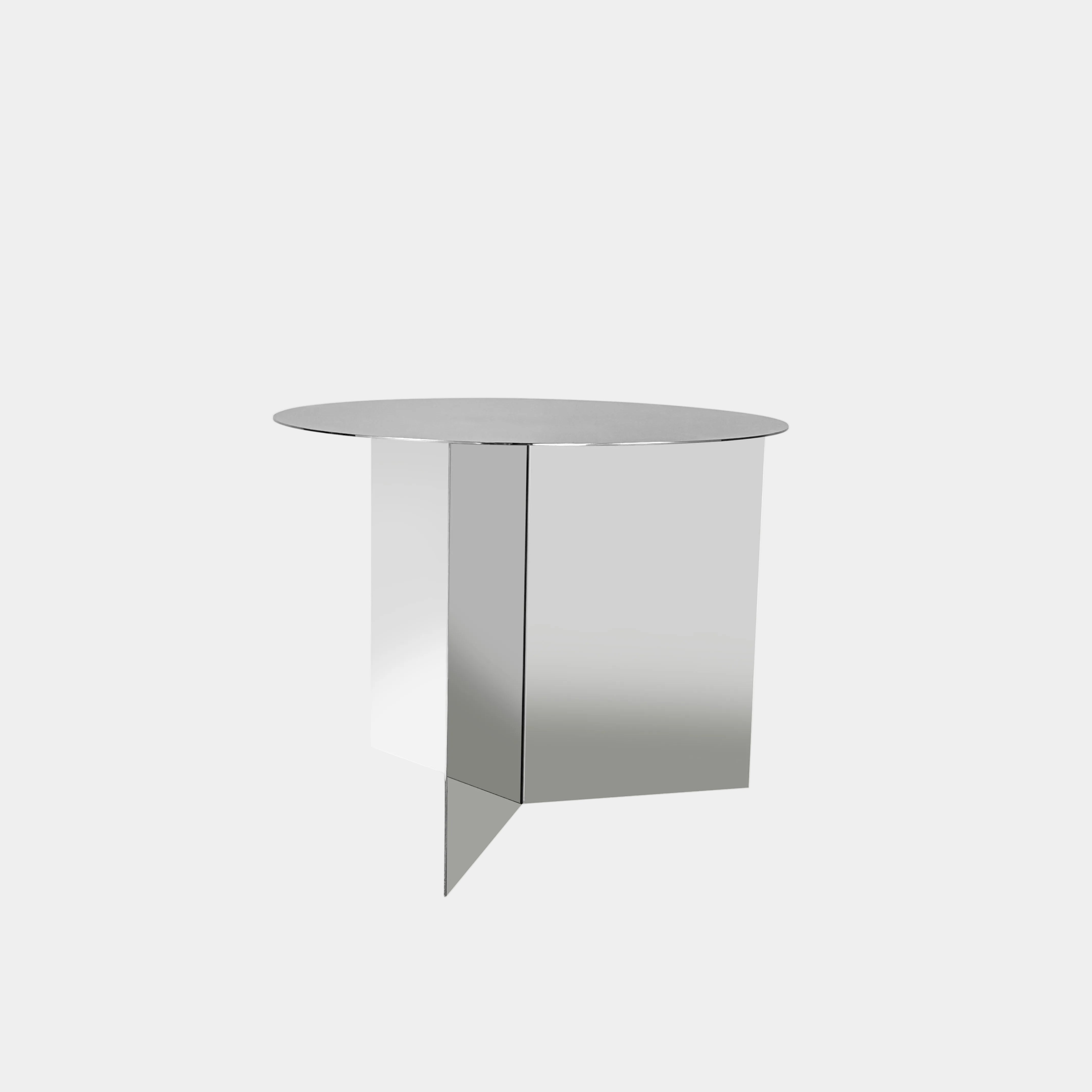 The Hay Slit Side Table by Hay features a round, reflective design with mirrored sides and is shown atop a dark wooden surface against a plain white wall.