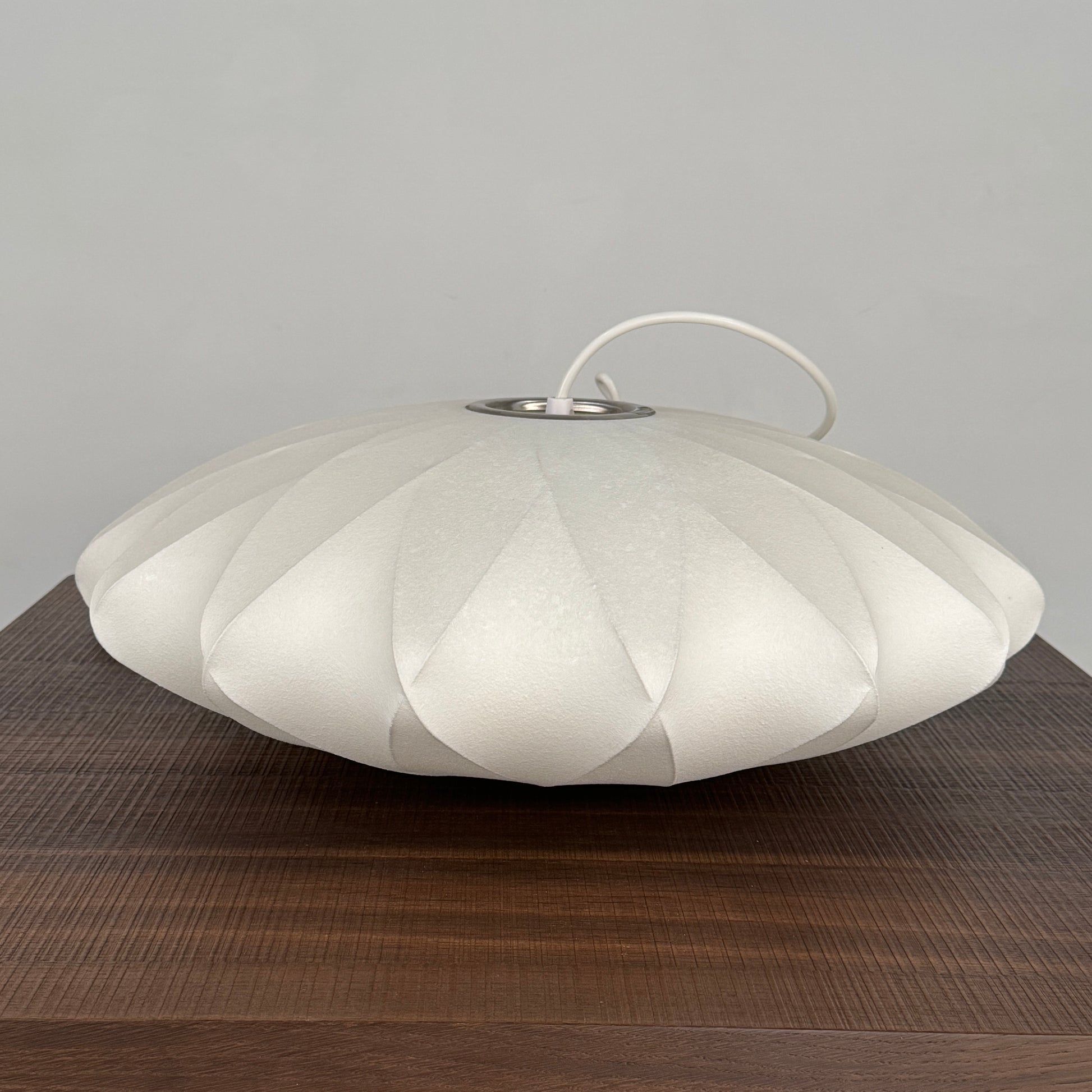 A medium Herman Miller Nelson Saucer Crisscross Bubble Pendant in white hangs before a wooden slat partition and beige sofa.