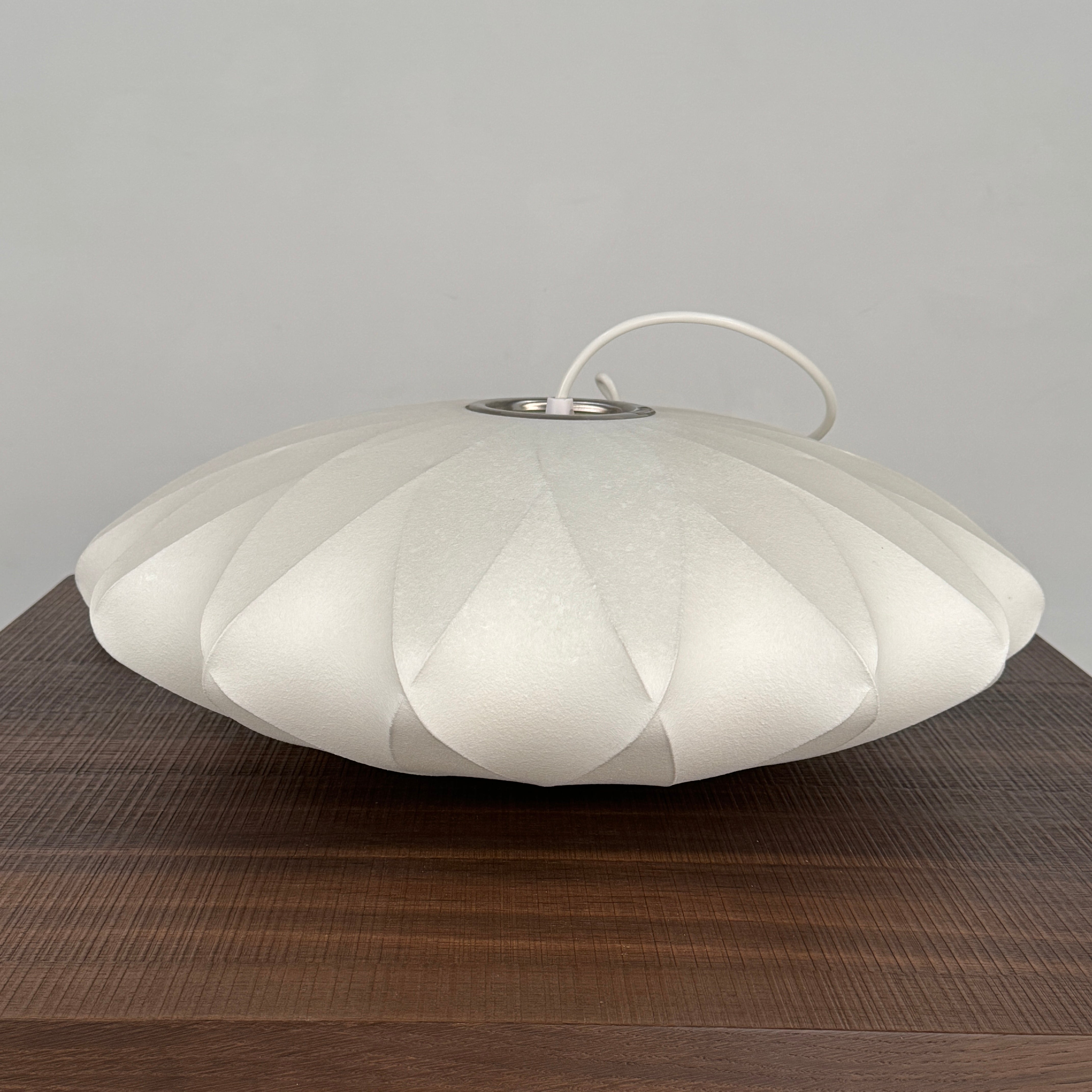 A medium Herman Miller Nelson Saucer Crisscross Bubble Pendant in white hangs before a wooden slat partition and beige sofa.