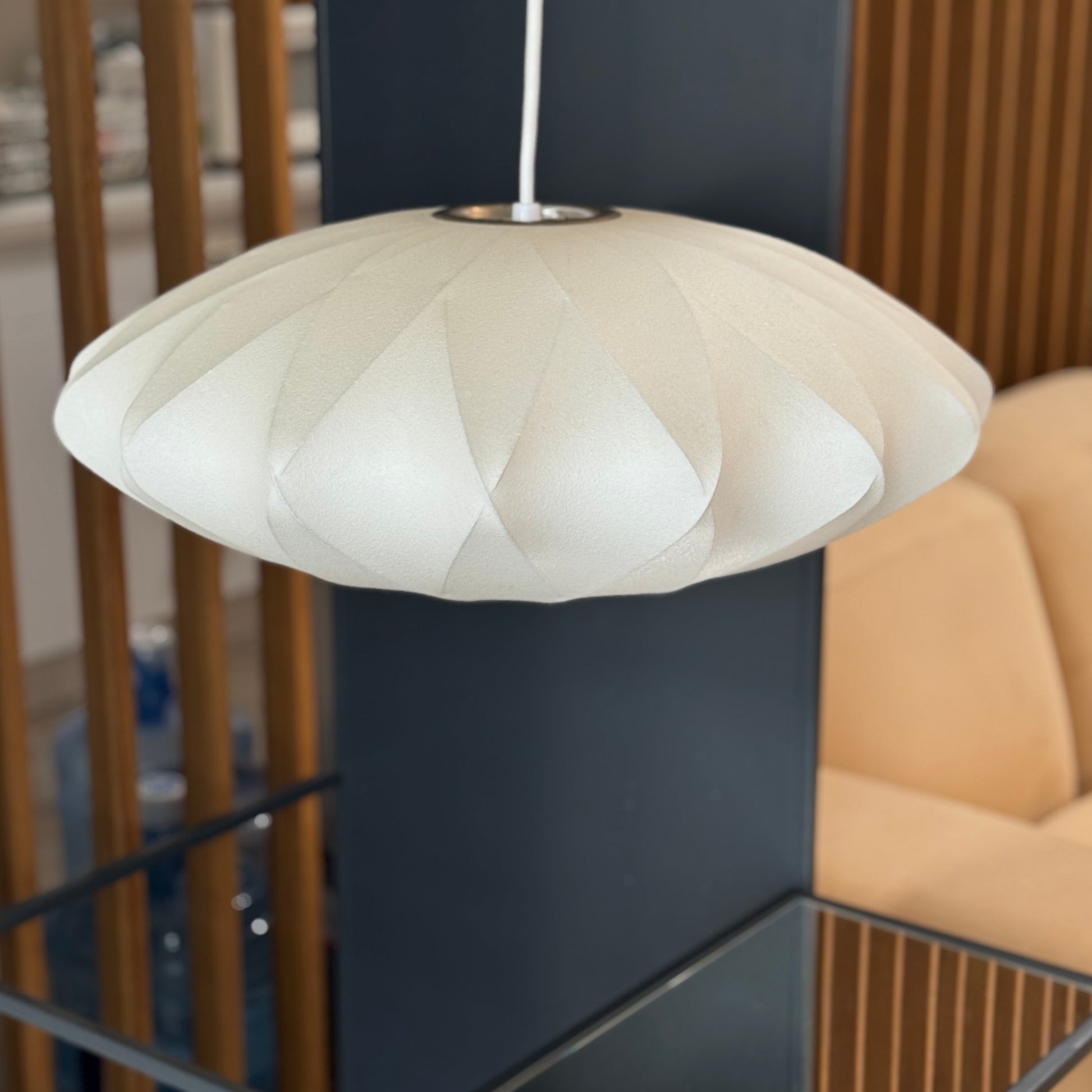 A medium Herman Miller Nelson Saucer Crisscross Bubble Pendant in white hangs before a wooden slat partition and beige sofa.