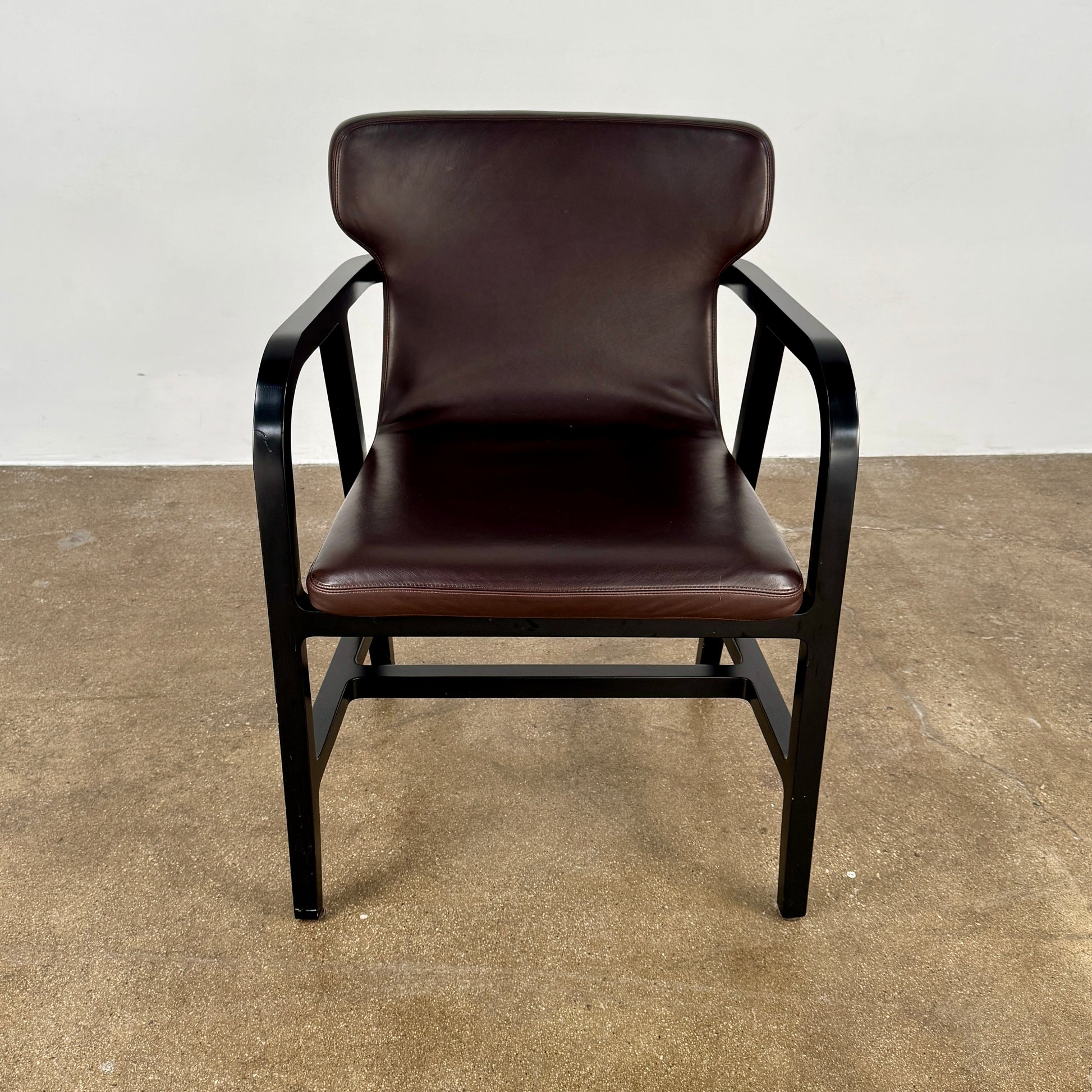 A pair of Maxalto Fulgens Armchair set (2) by Maxalto, in dark brown leather with black wooden frames, are placed side by side against a plain white background.