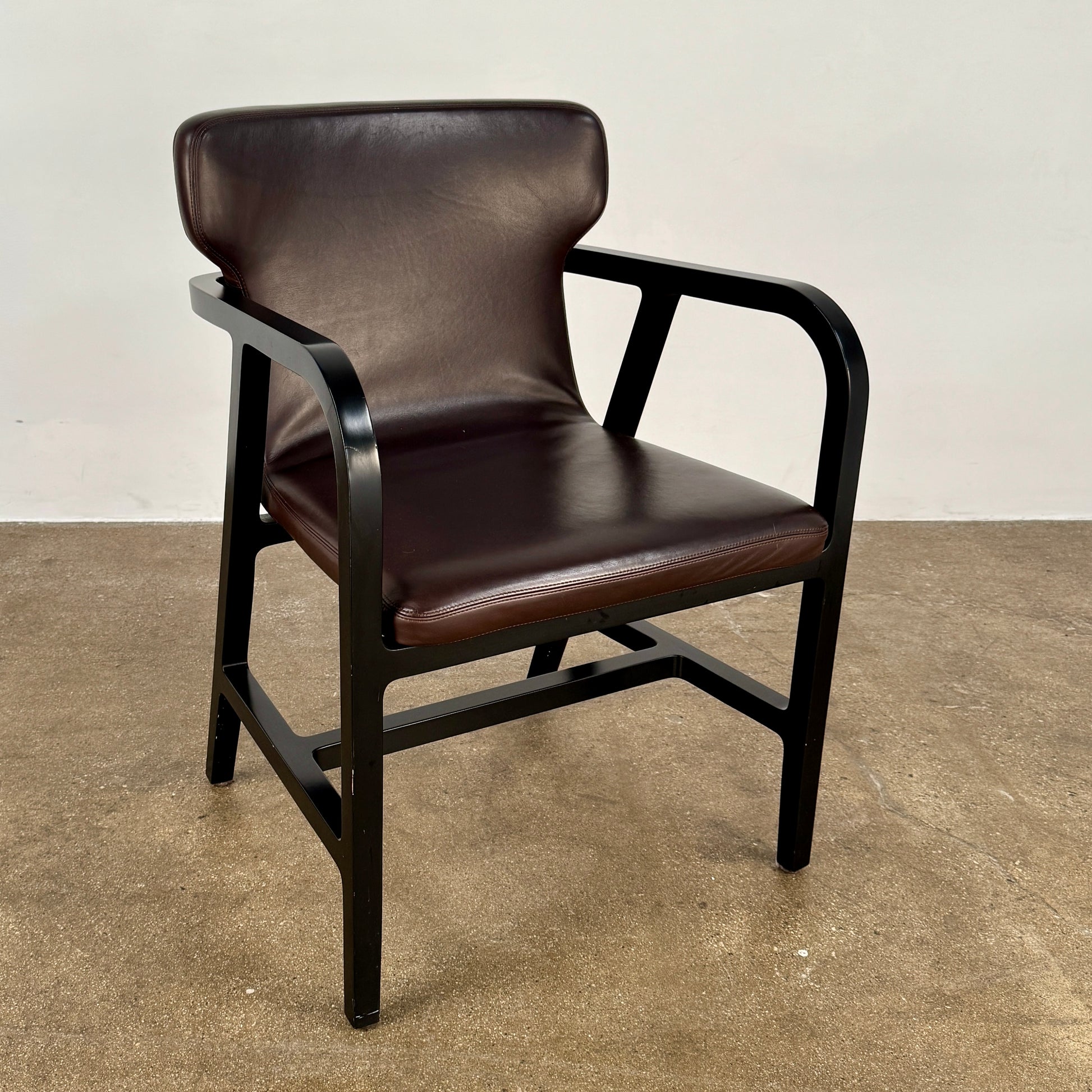 A pair of Maxalto Fulgens Armchair set (2) by Maxalto, in dark brown leather with black wooden frames, are placed side by side against a plain white background.
